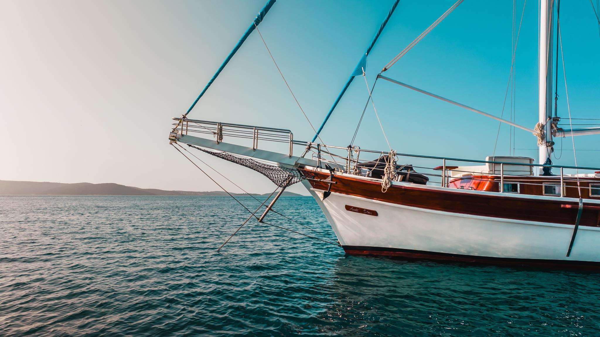 white hull traditional gulet with wooden deck and rigging anchored in turquoise waters