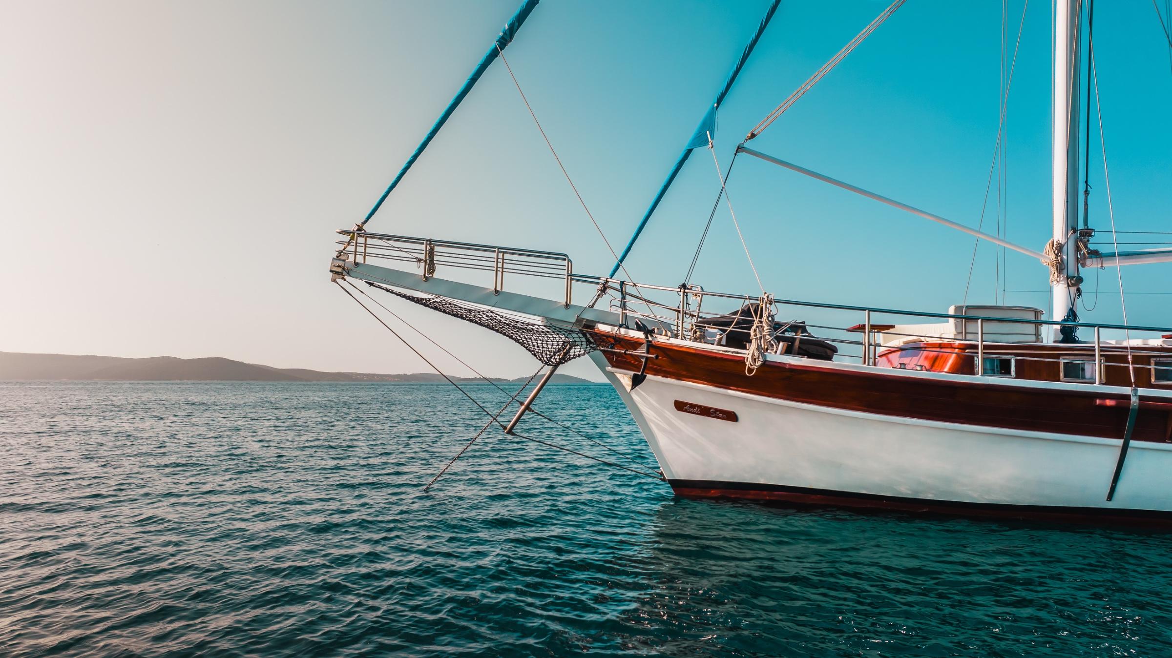 white hull traditional gulet with wooden deck and rigging anchored in turquoise waters