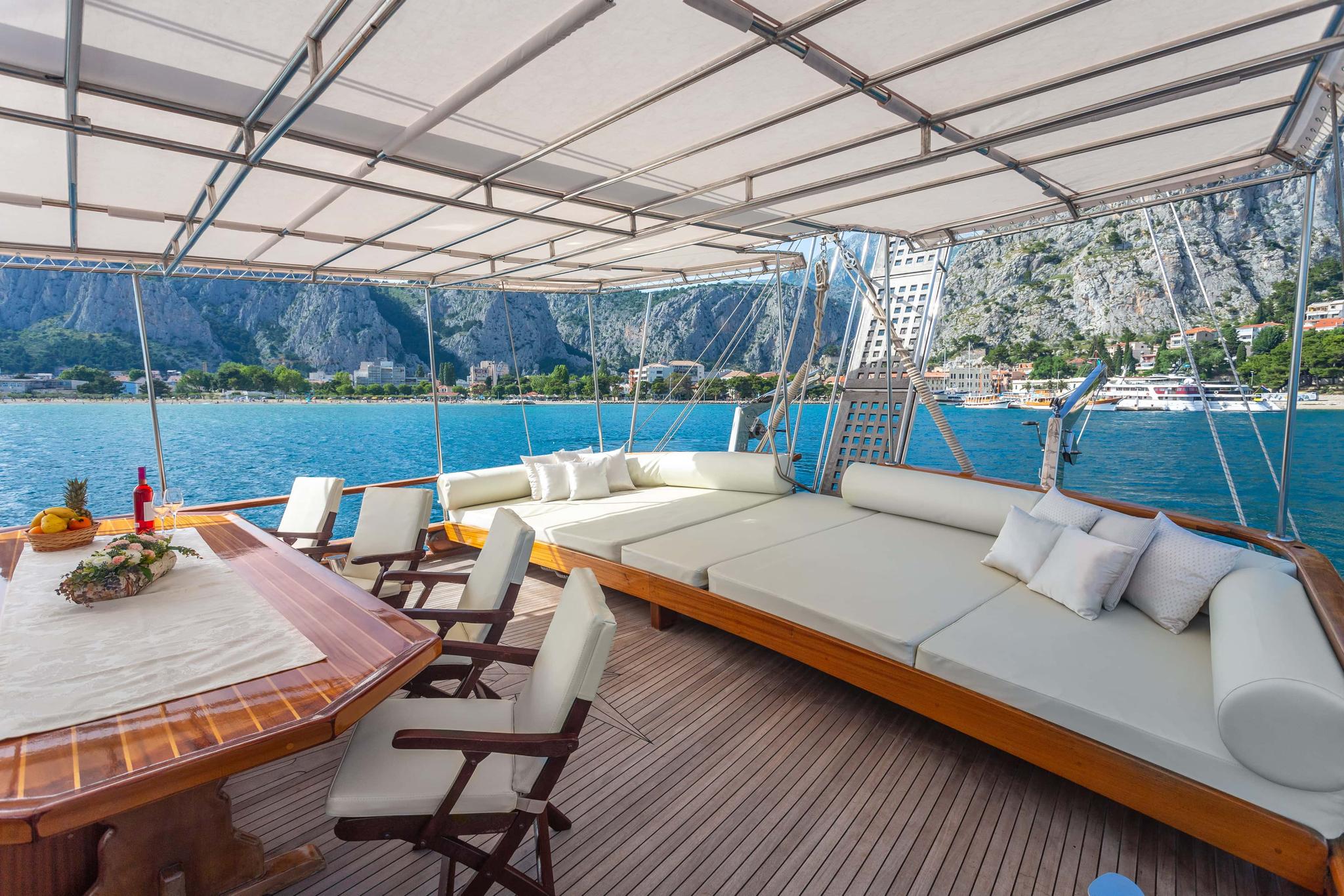 Covered aft deck with curved seating, dining table and scenic bay views