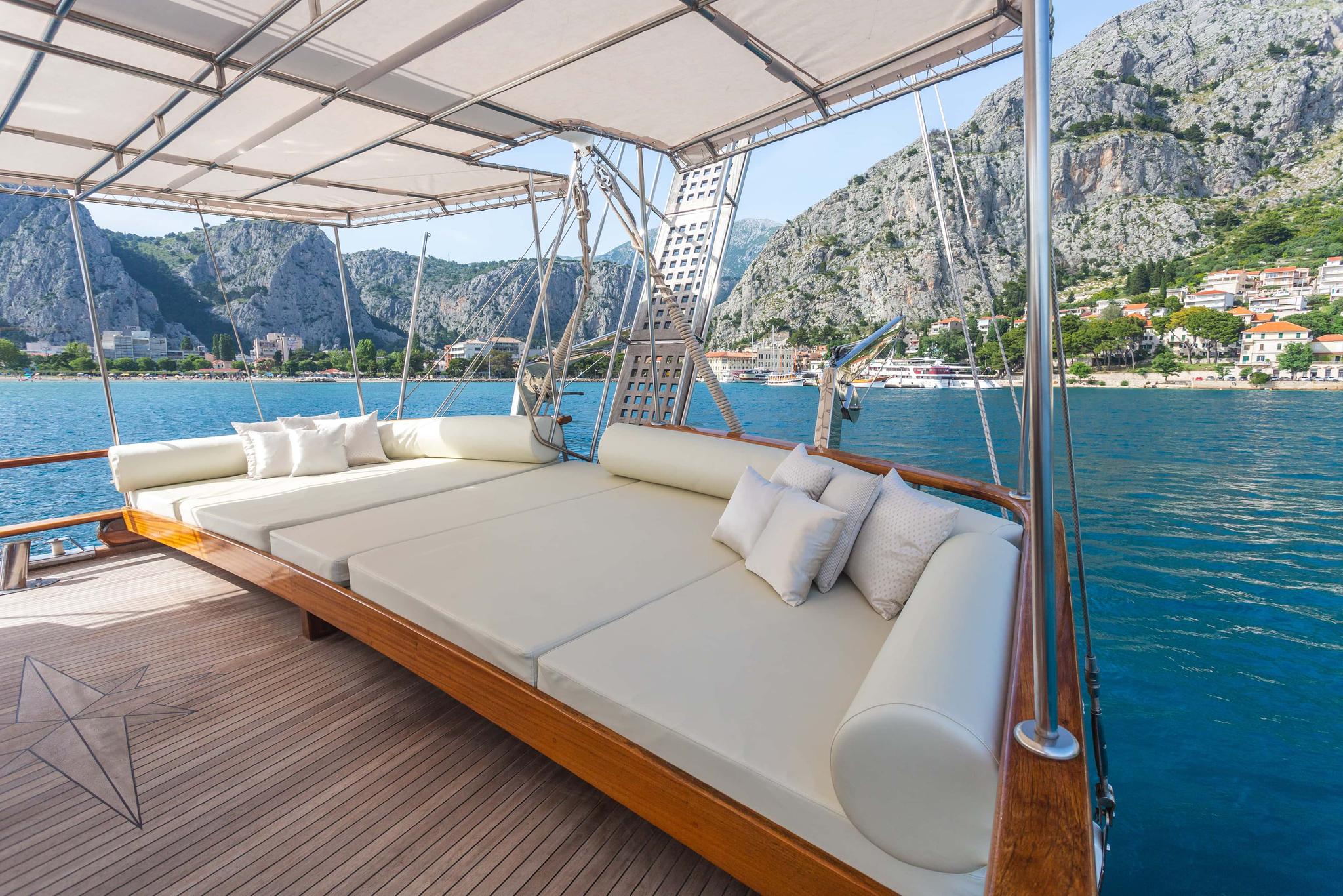 yacht aft deck with large cushioned daybed seating and fabric canopy overlooking coastal bay