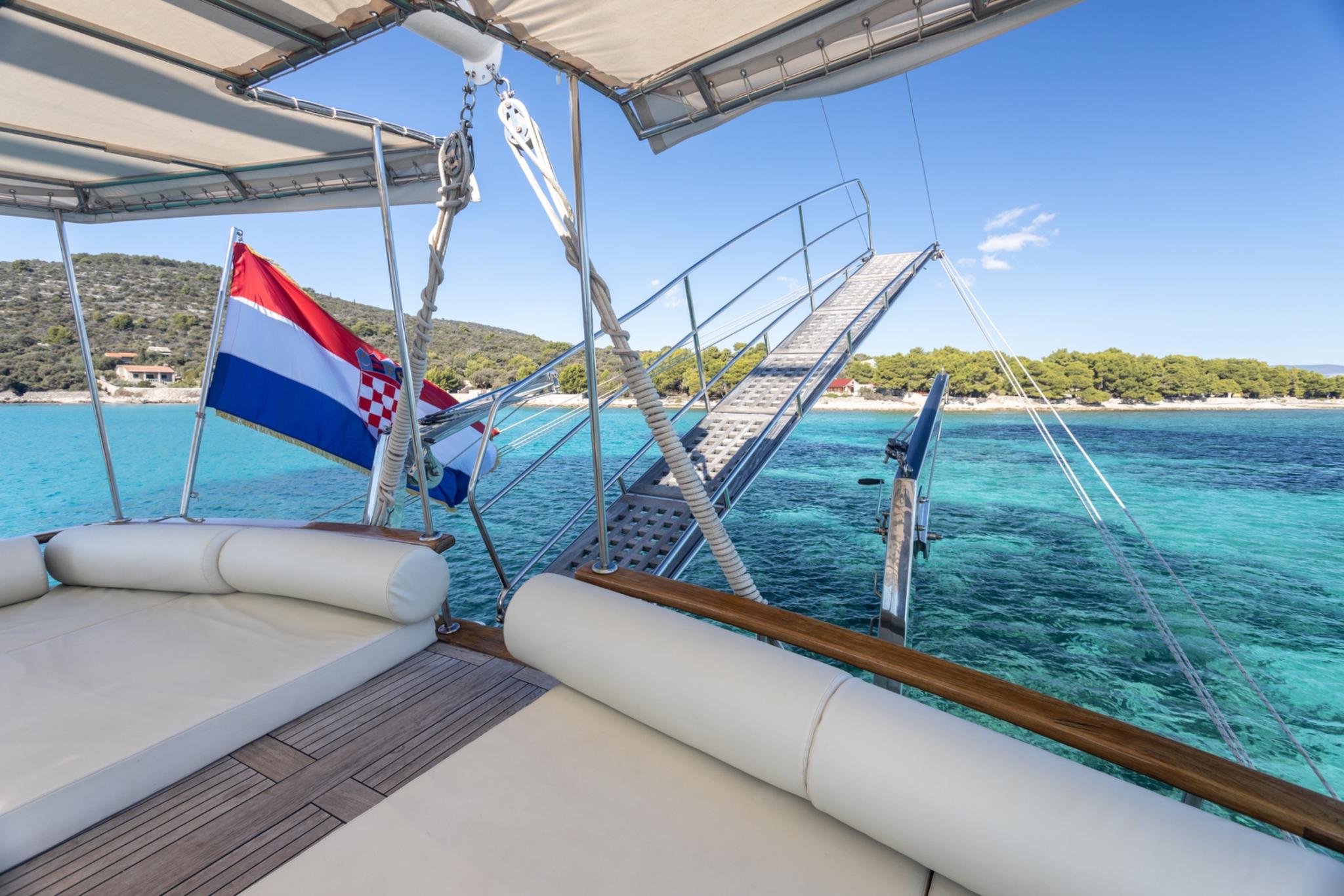yacht aft deck with white cushioned seating, Croatian flag, and crystal clear turquoise waters