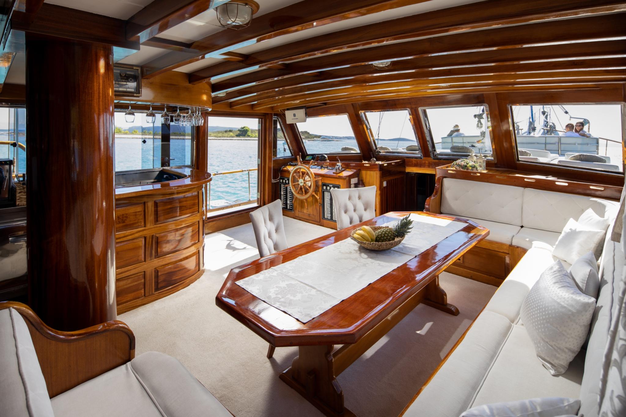 yacht main salon interior with wooden dining table, white upholstered seating, and helm area