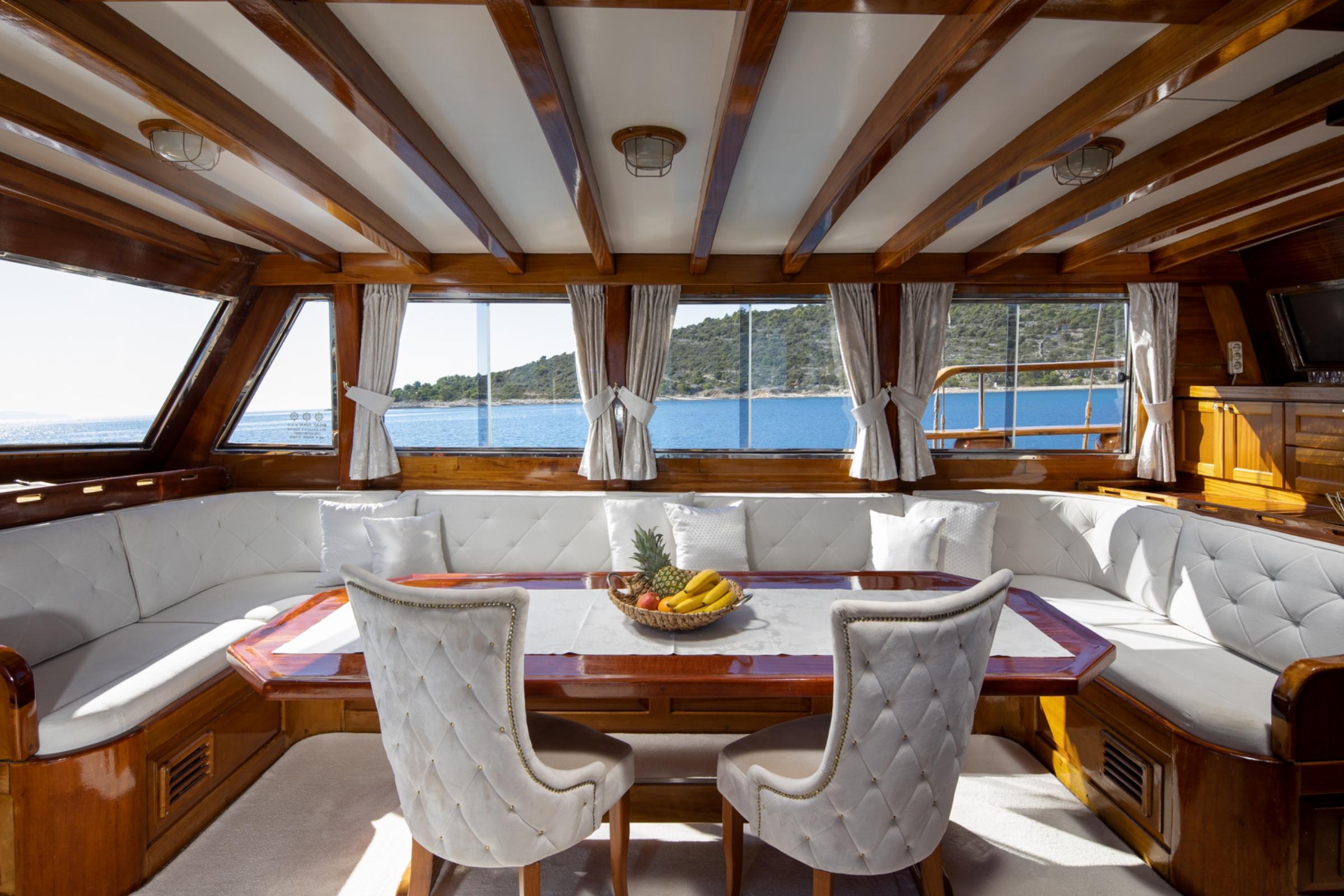 gulet salon interior with white U-shaped banquette seating, wooden dining table, and panoramic windows