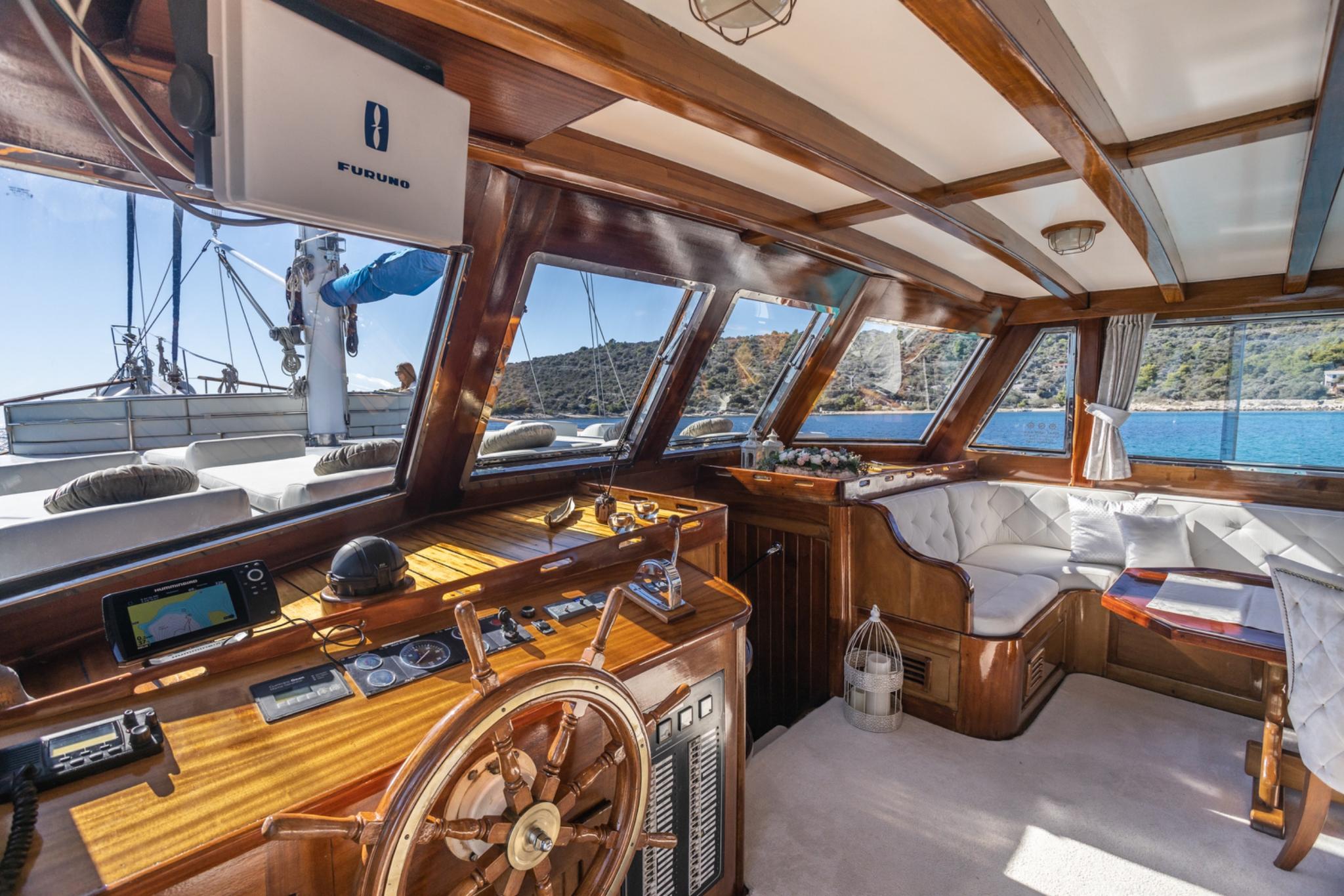 yacht wheelhouse interior with traditional wooden steering wheel, navigation equipment, and white cushioned seating