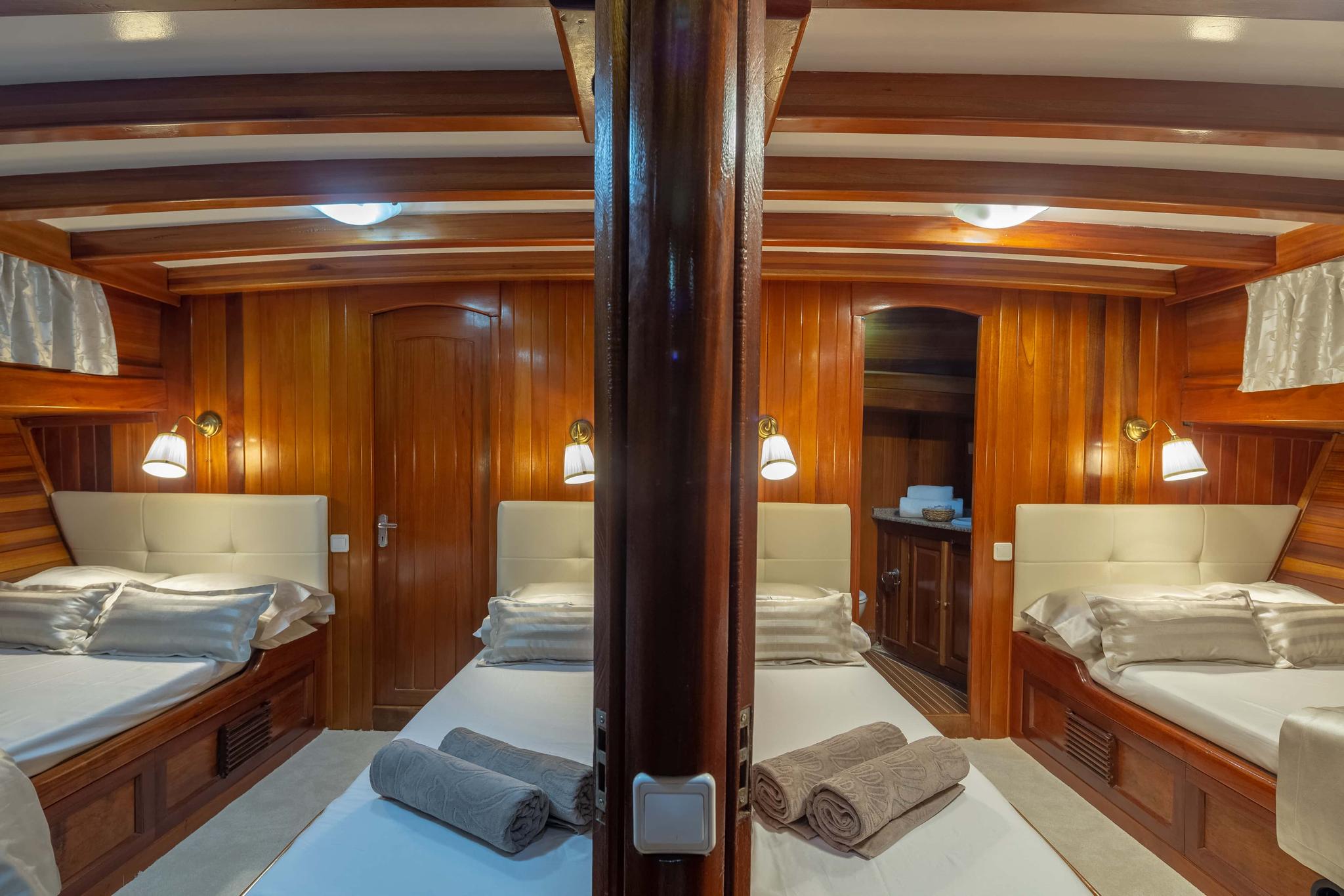 yacht twin cabin interior with four single beds, cream upholstery, and central wooden mast