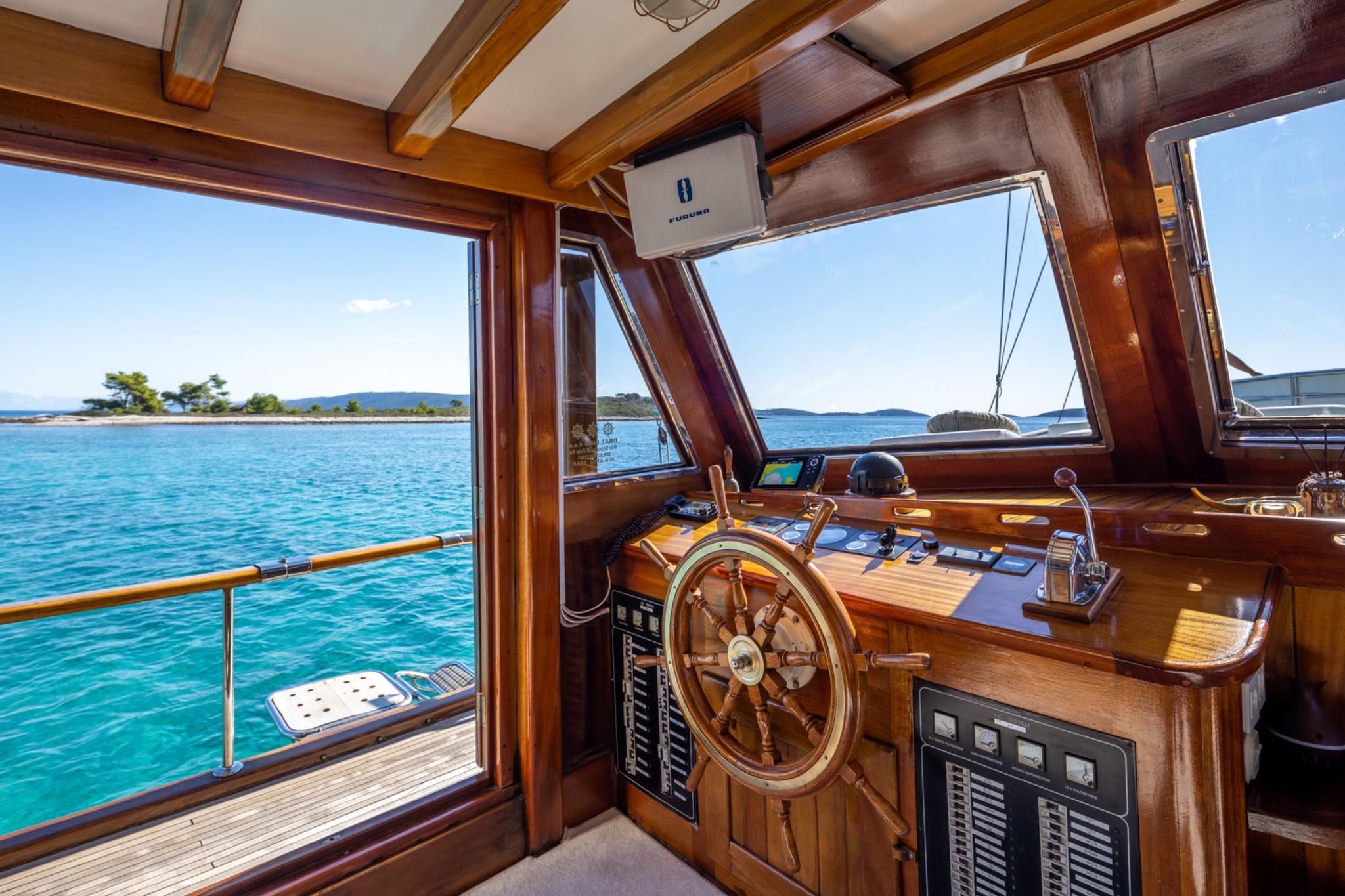 yacht wheelhouse interior with wooden helm wheel and navigation controls overlooking turquoise waters