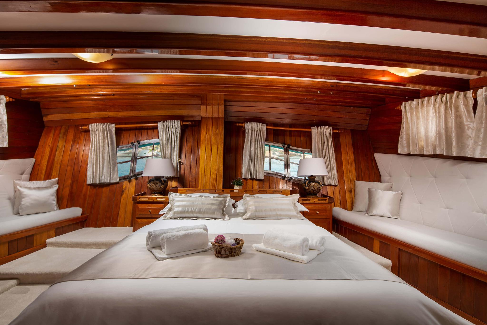 yacht guest cabin with double bed, built-in bench seating, wooden paneling and portholes