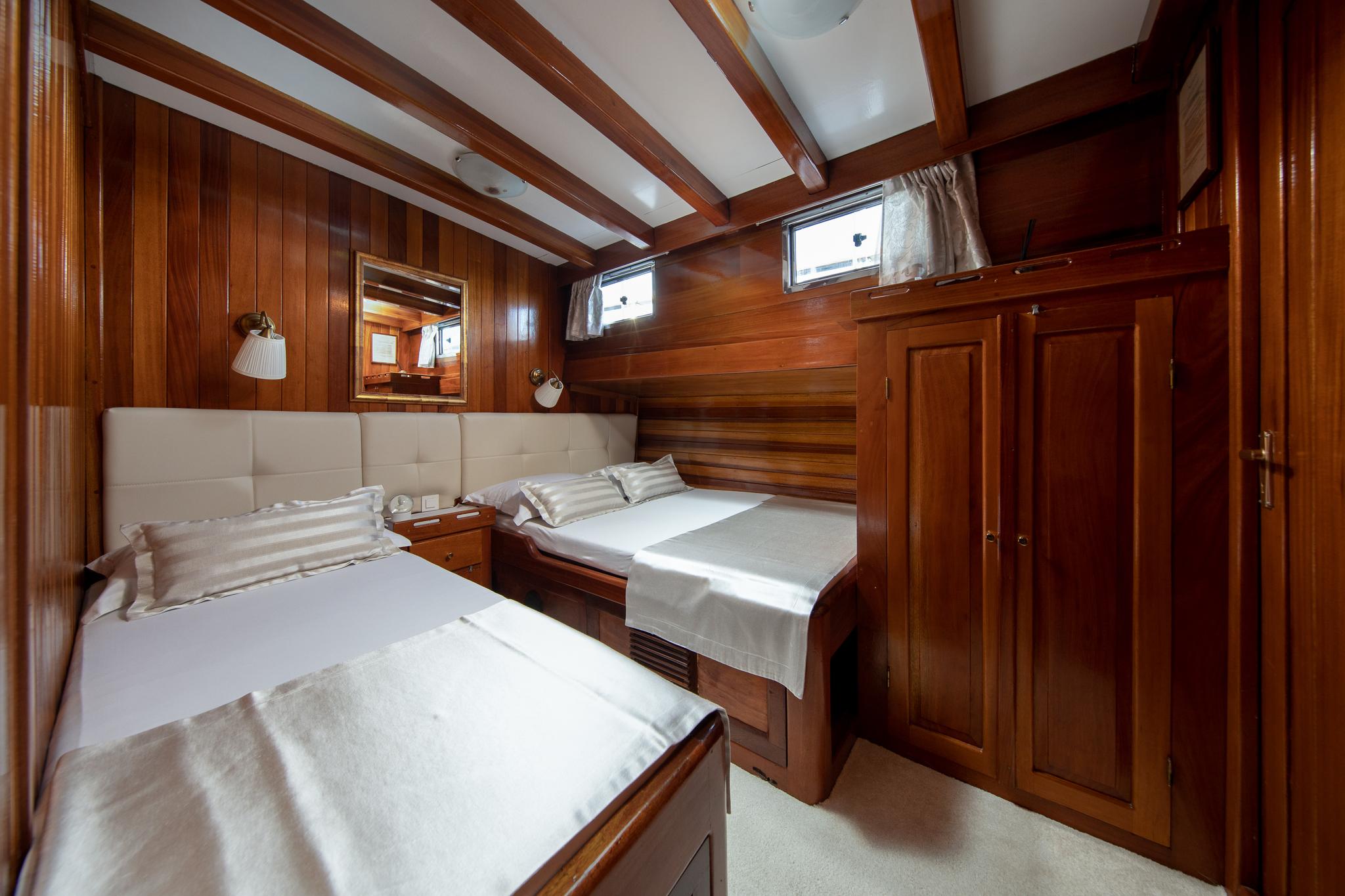 luxury yacht twin cabin with two single beds, cream upholstered headboard and rich wood paneling