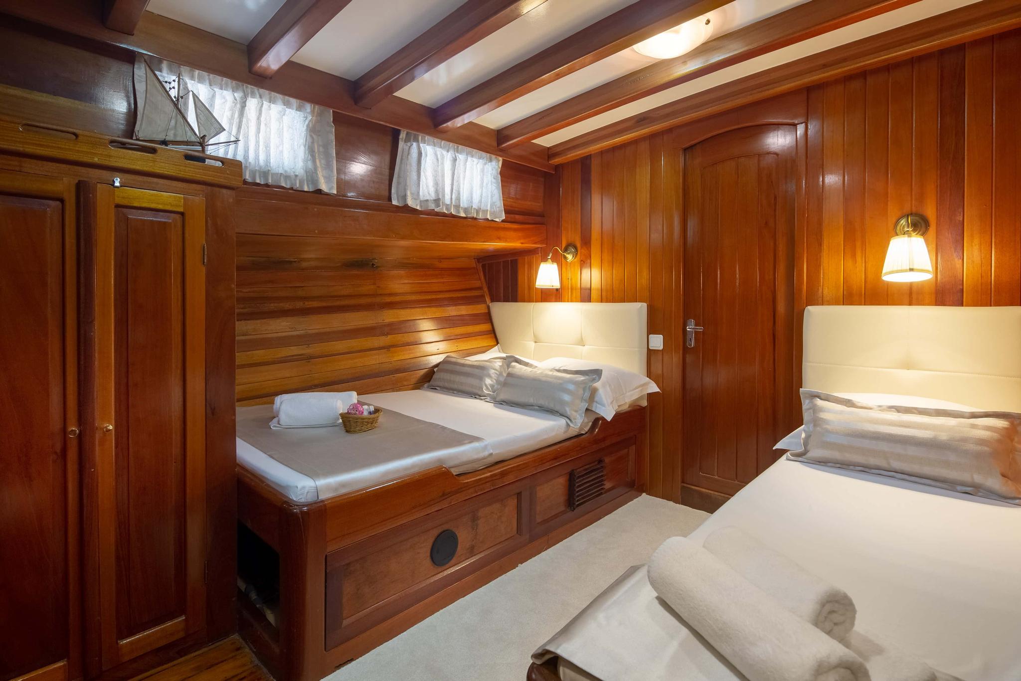 twin bed guest cabin with rich wood paneling, white upholstery and small portholes