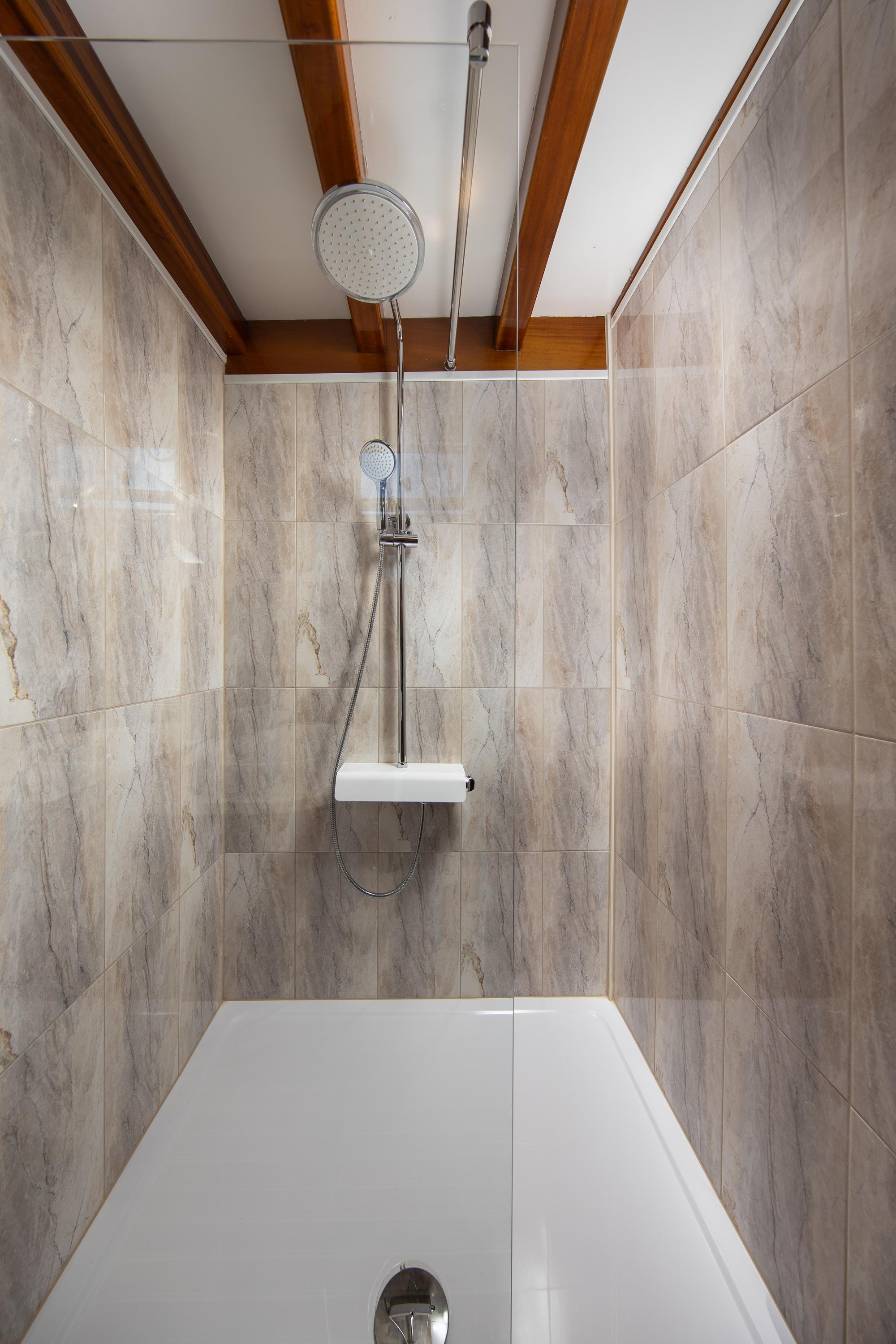yacht bathroom featuring marble-effect tiled walls, rainfall shower system, and white rectangular bathtub