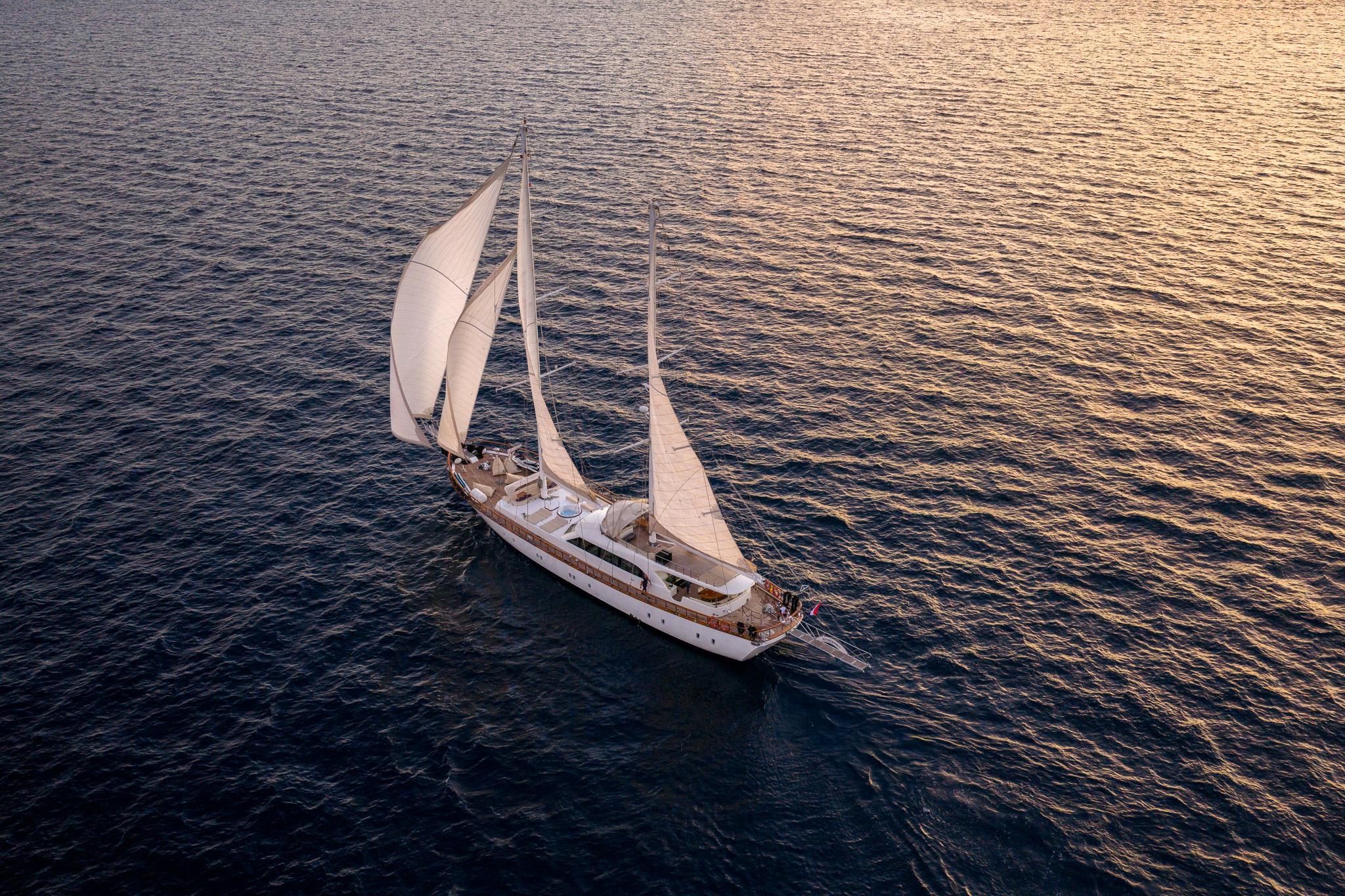 aerial view of white sailing gulet with cream sails on calm sea at sunset