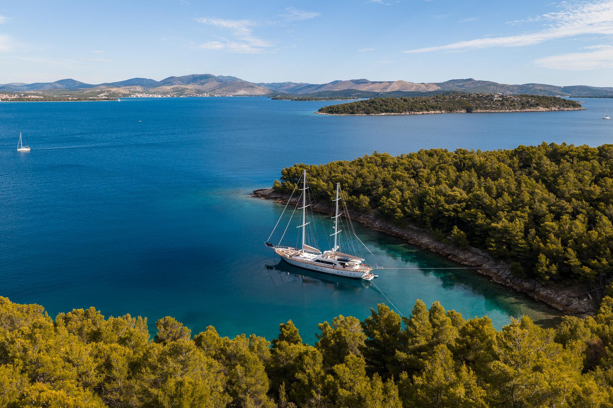 aerial view of luxury gulet anchored in pristine turquoise bay surrounded by pine forest