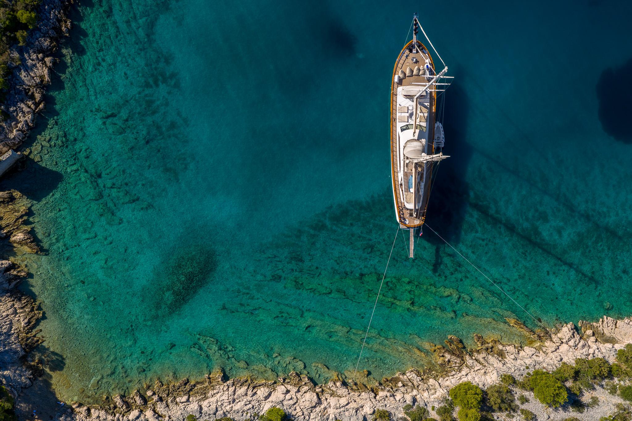 aerial view of wooden gulet yacht anchored in crystal clear turquoise bay near rocky coastline