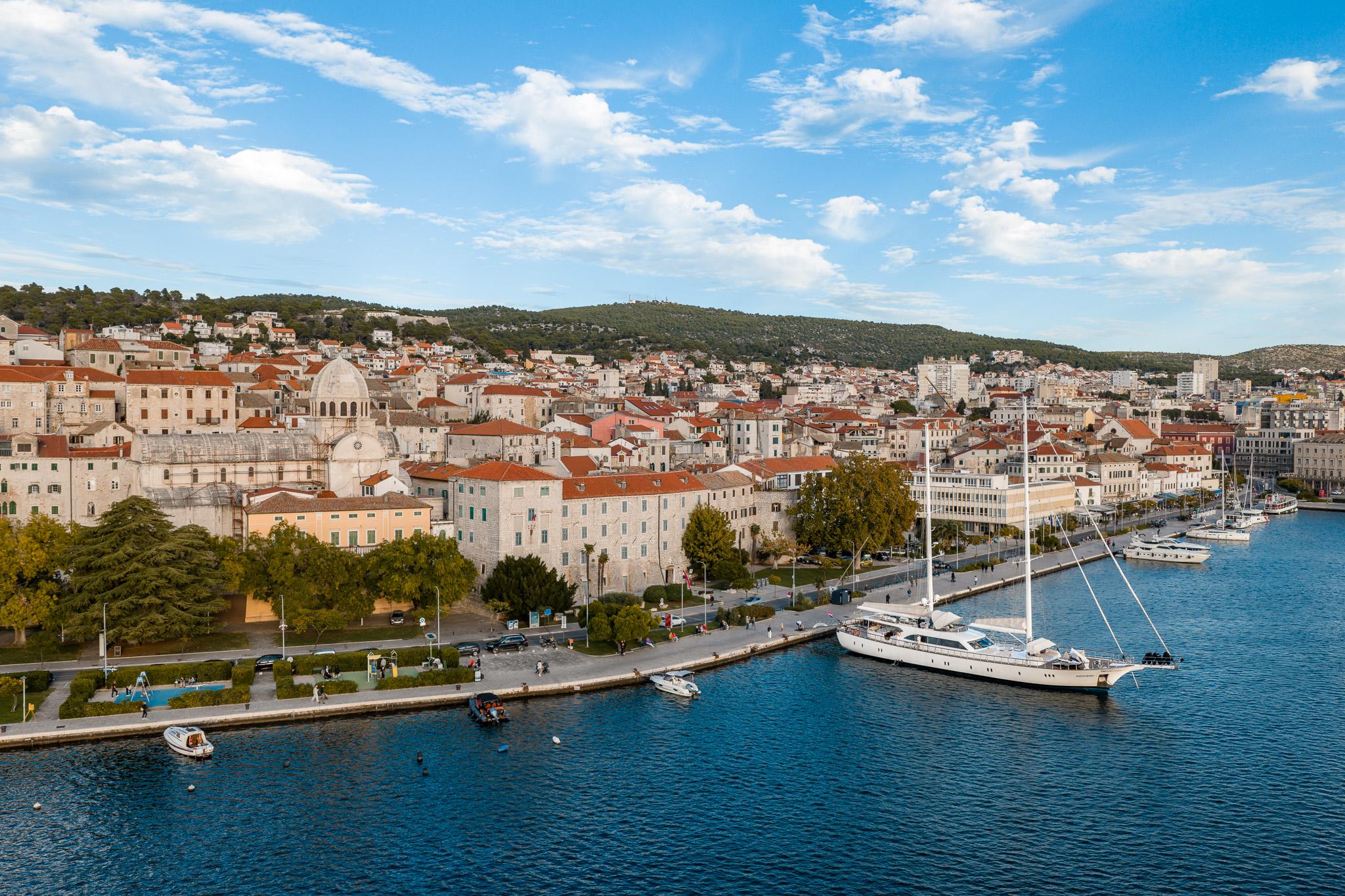 aerial view of Mediterranean coastal town with white sailing yacht moored at waterfront promenade