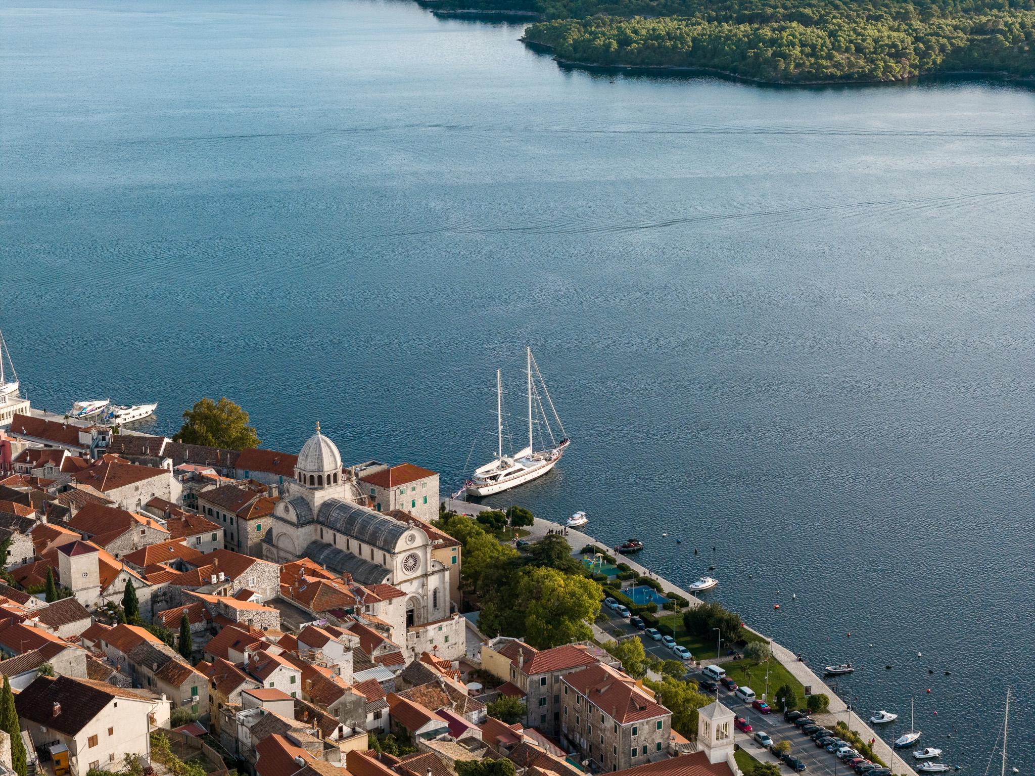 aerial view of historic coastal town with white sailing yacht anchored in blue bay