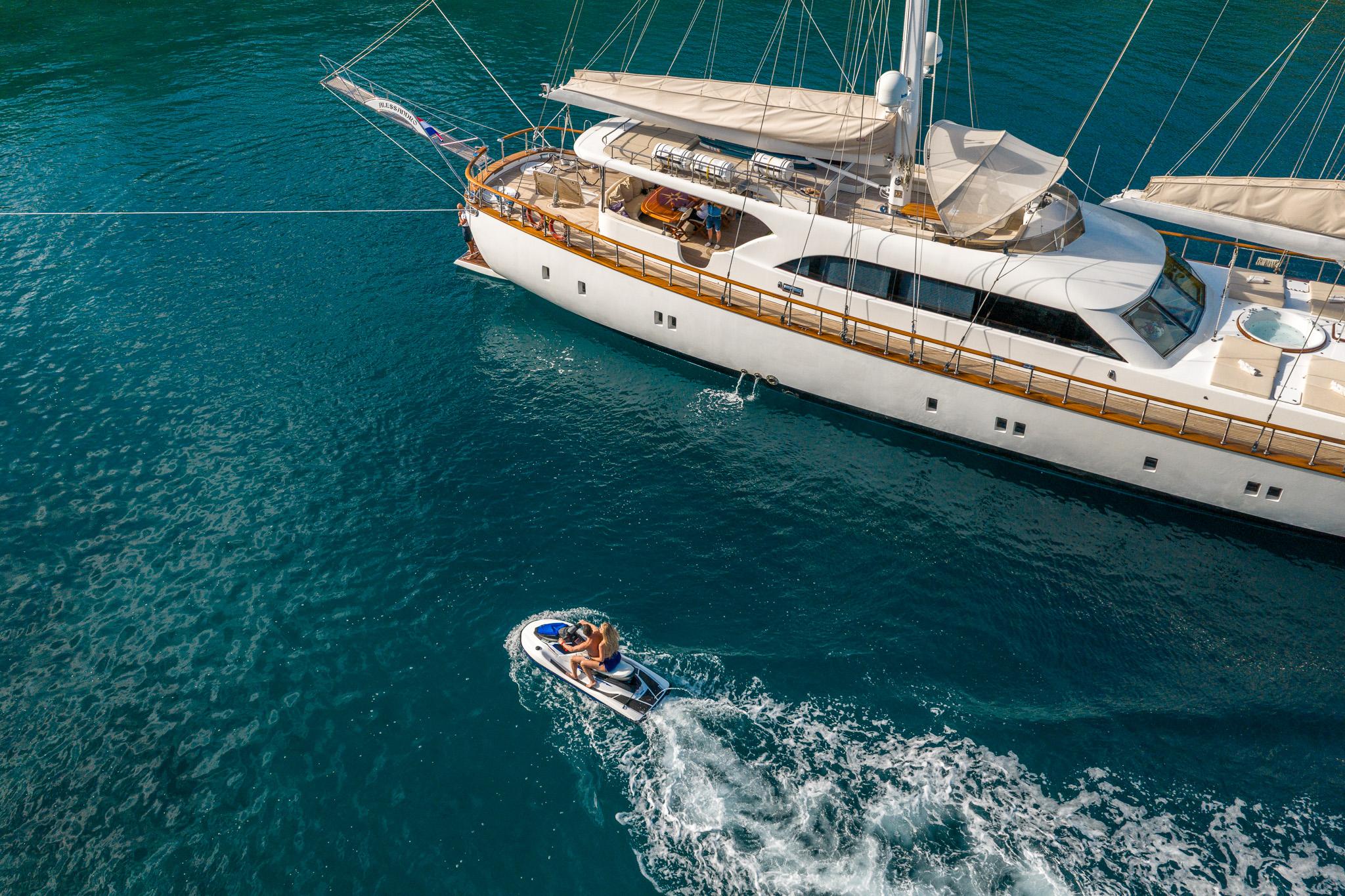 aerial drone shot of white luxury gulet yacht anchored in turquoise waters with tender boat nearby