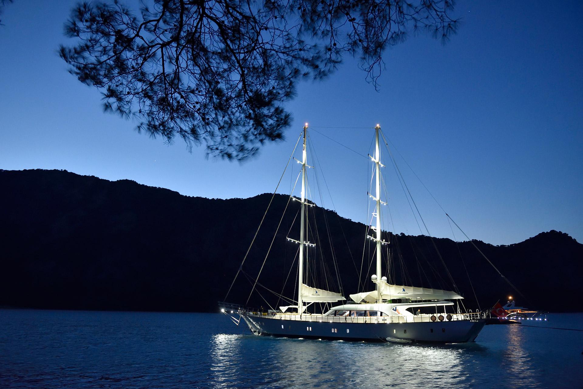 white gulet yacht anchored in bay at twilight with illuminated masts and rigging