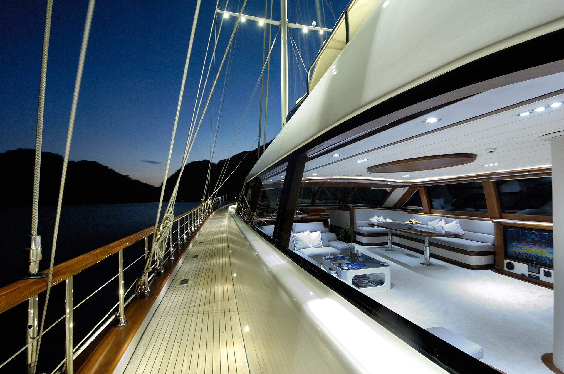 luxury yacht side deck with white cushioned seating area and coffee table at evening