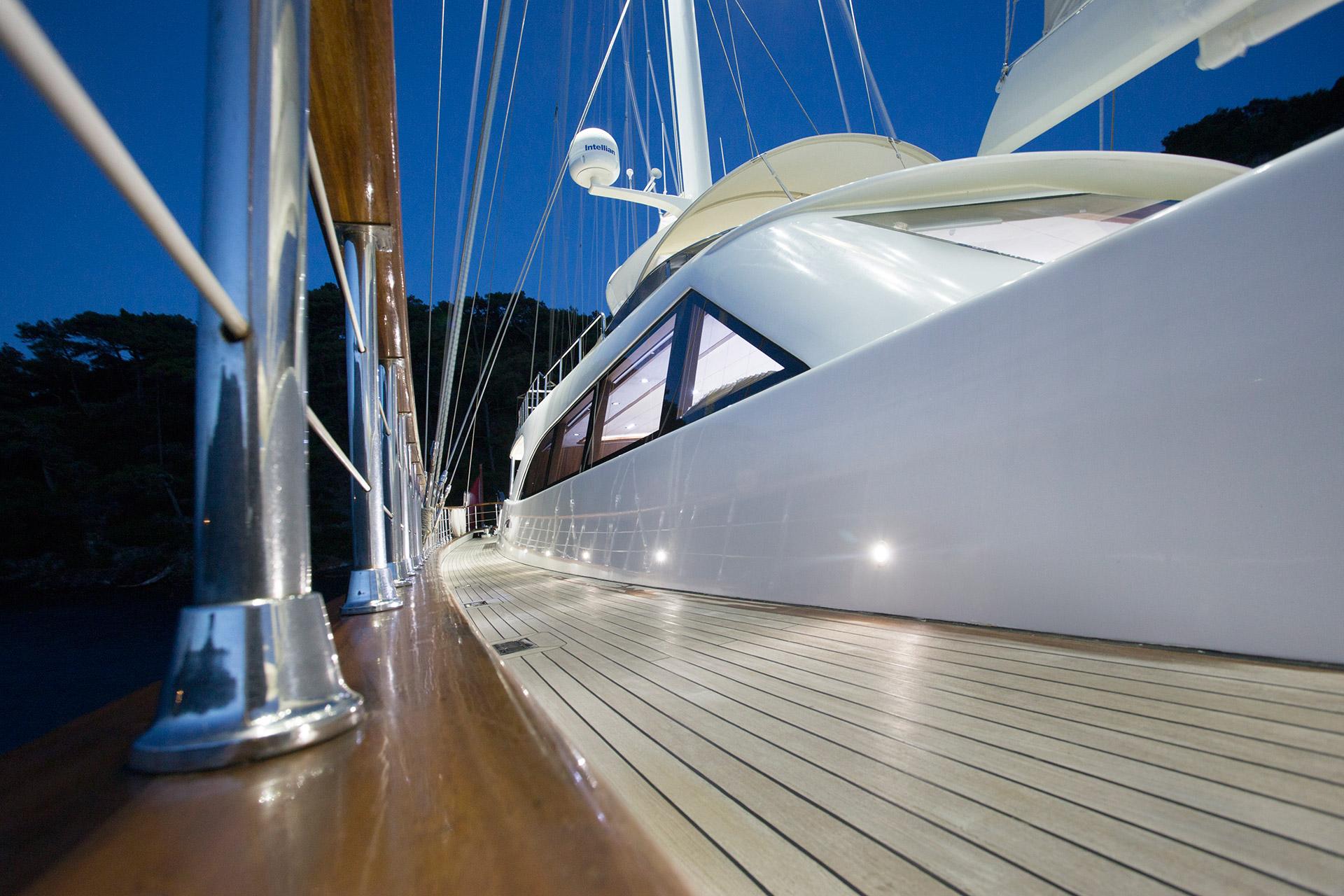 yacht side deck with teak planking, white hull, rigging and mast visible at dusk