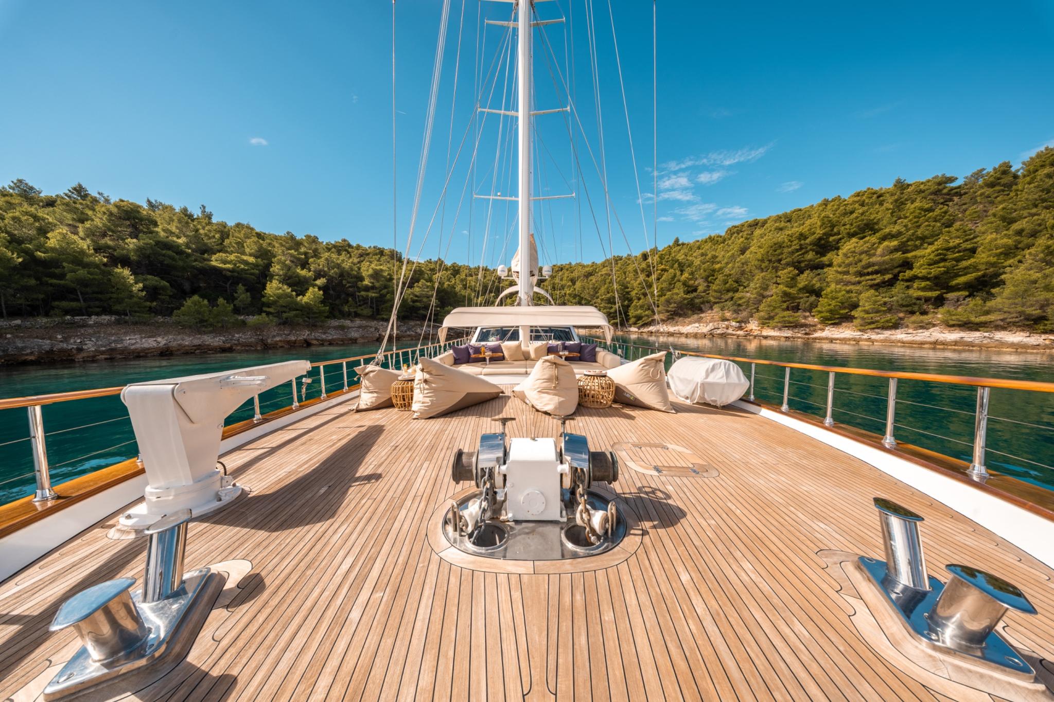 yacht bow deck with cushioned seating area, anchor windlass, and teak decking in Mediterranean bay