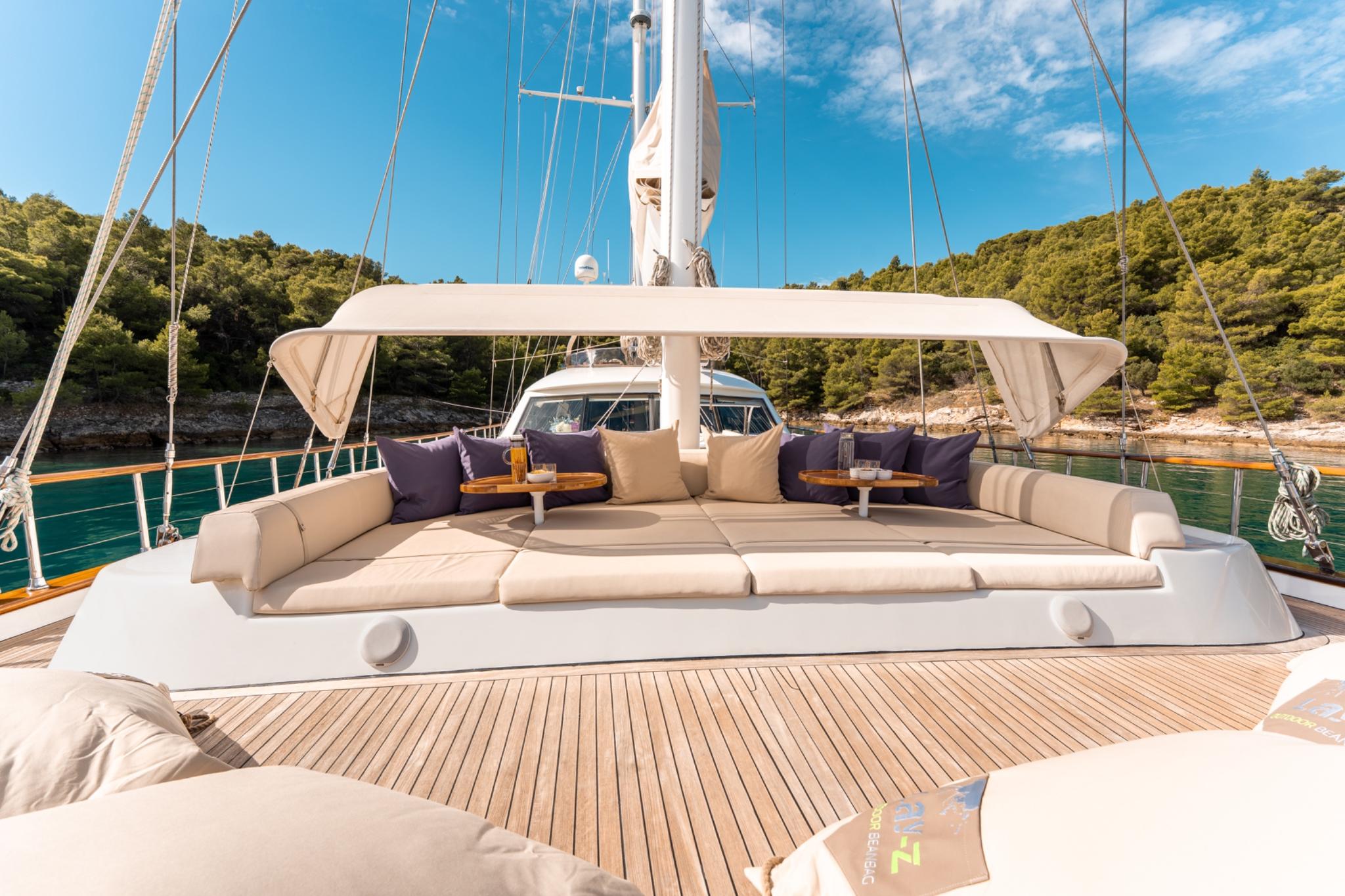 gulet forward deck with cream cushioned seating area and navy pillows under white awning