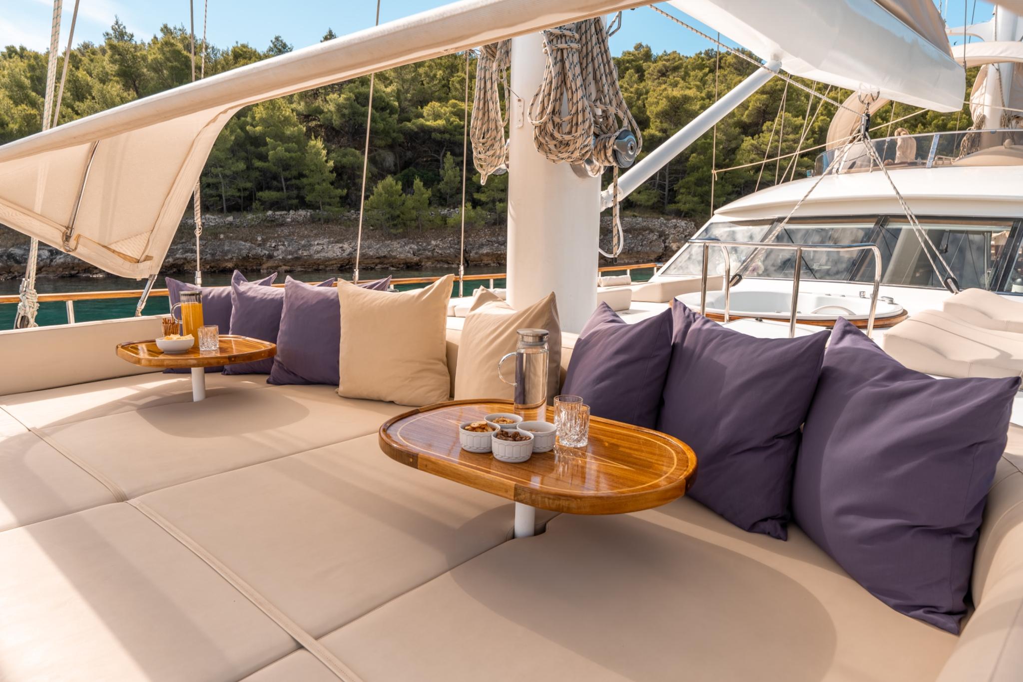 aft deck seating area with beige cushioned sofas, purple pillows and wooden tables