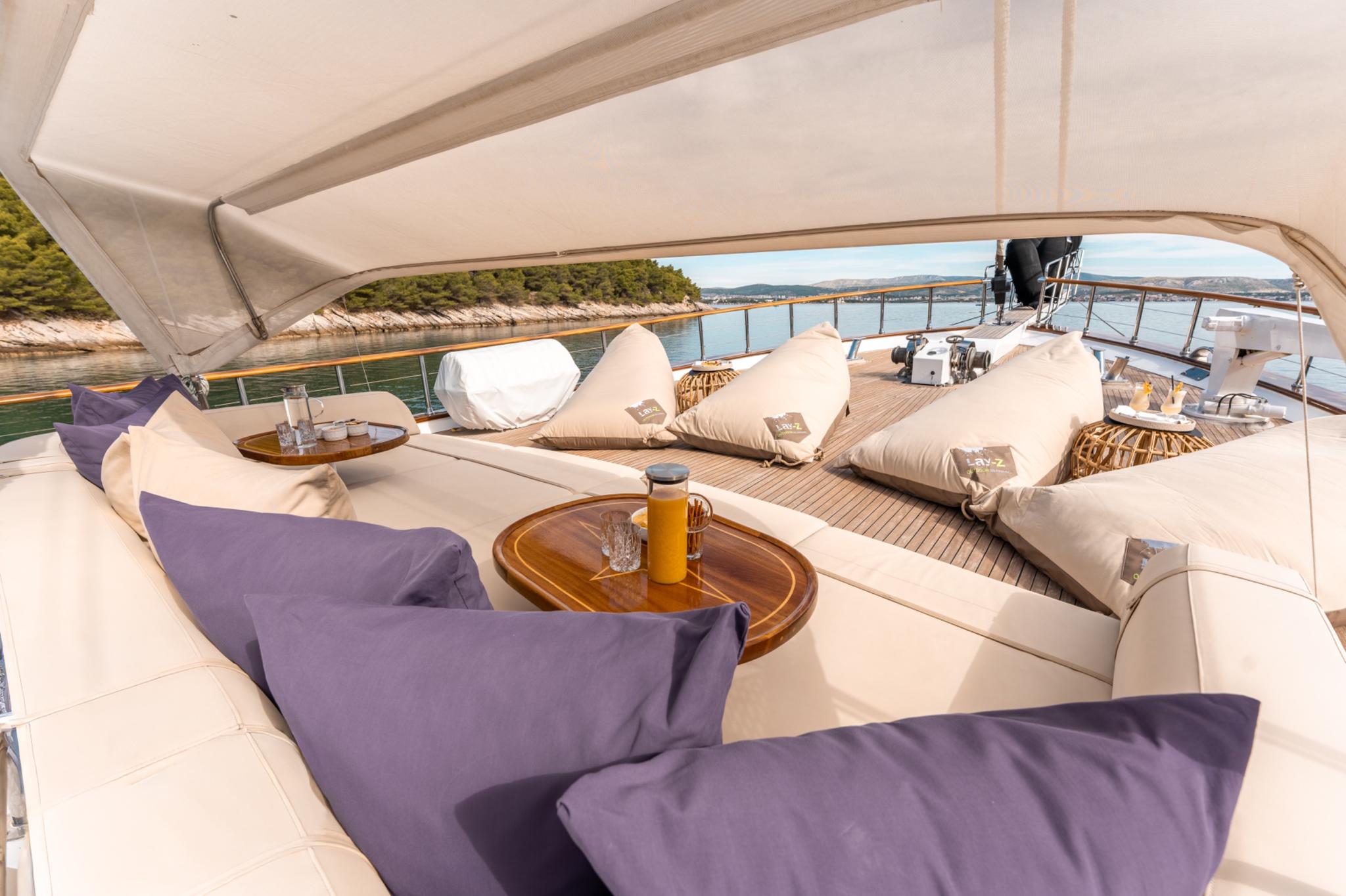 yacht aft deck lounge area with beige cushioned seating, purple pillows and wooden tables under awning