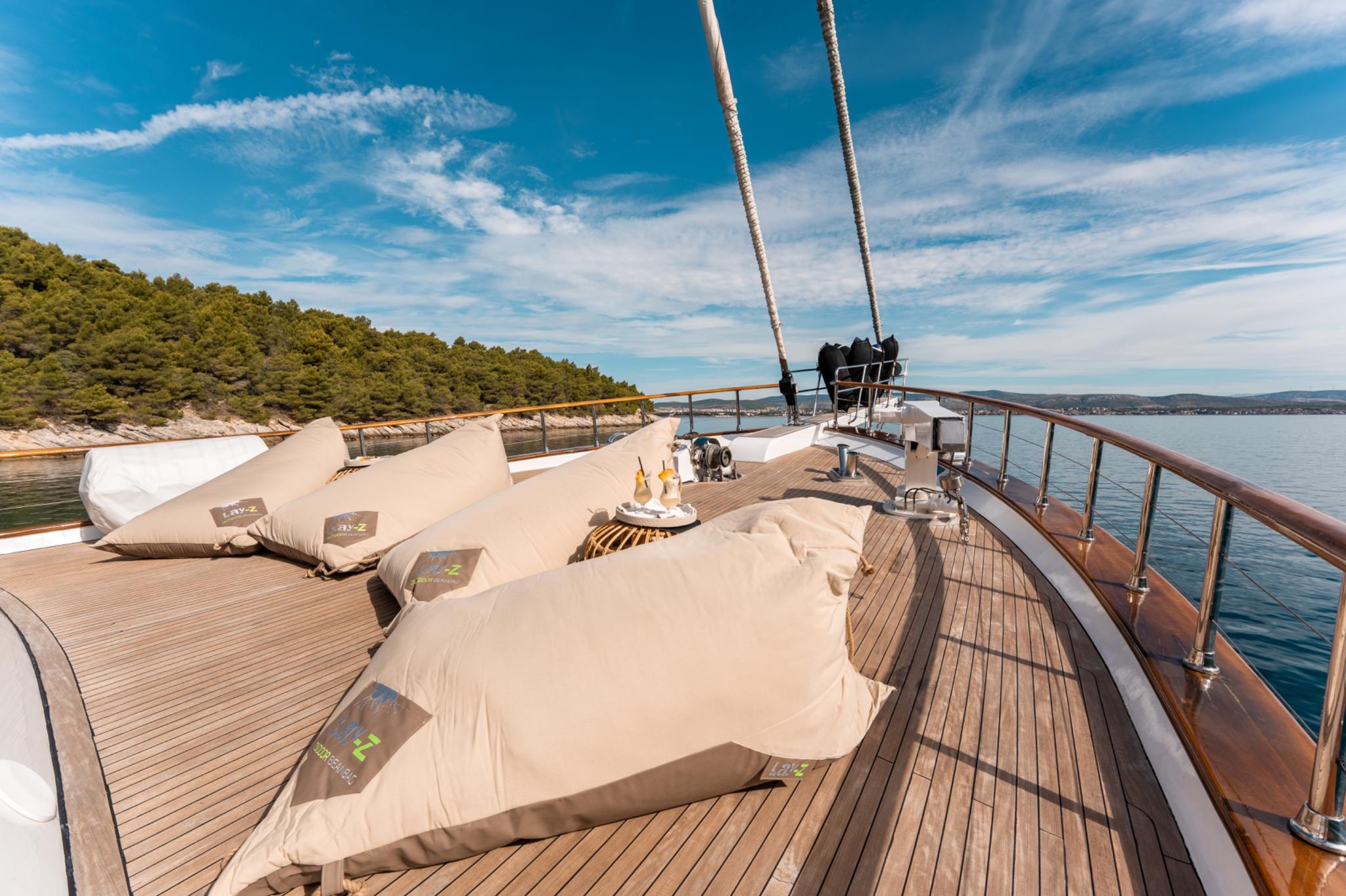 yacht bow deck with beige sun pads, teak decking, and mast rigging in coastal waters