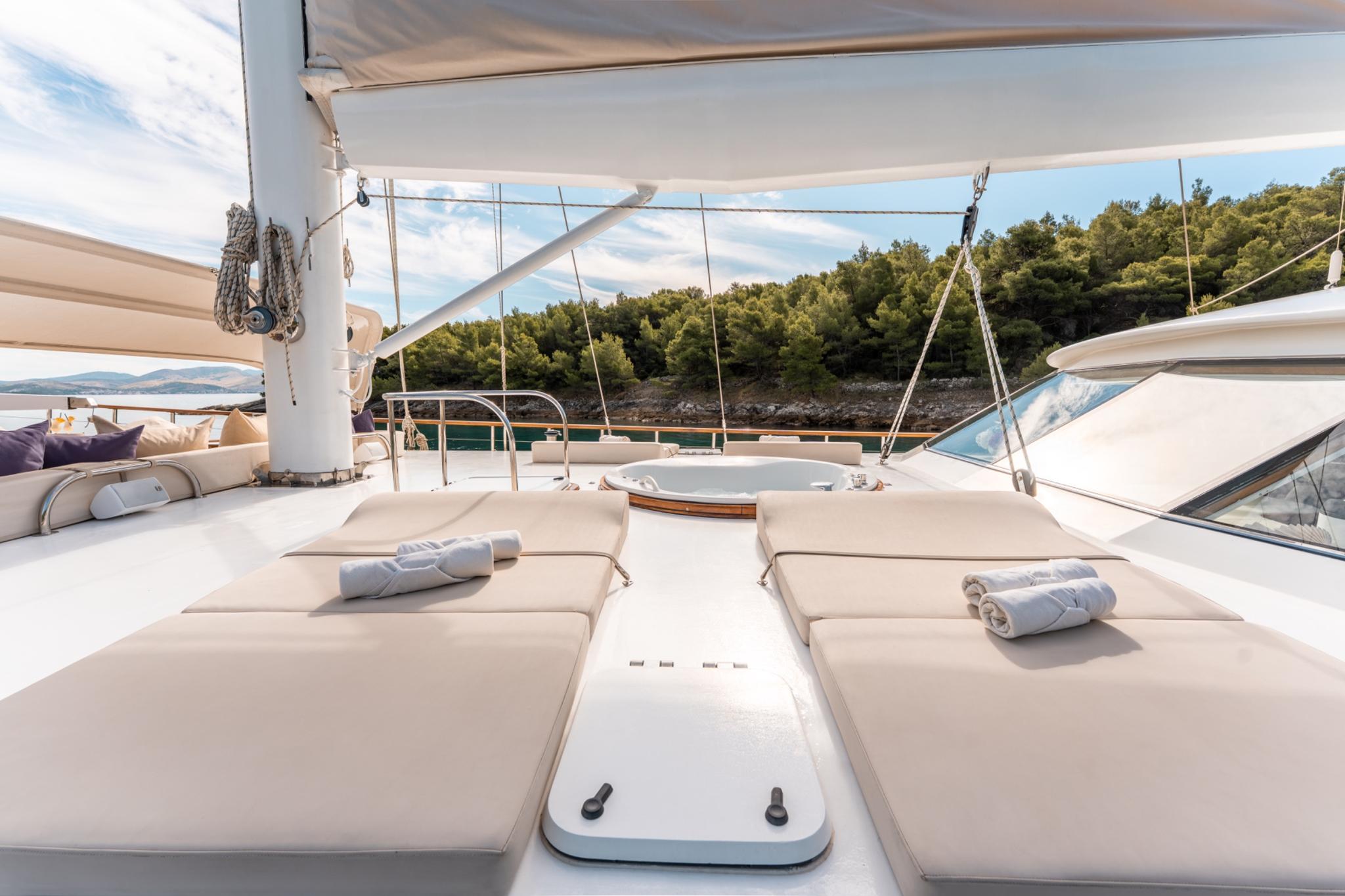 bow sun deck area with beige cushioned loungers, rolled towels, and white awning shade