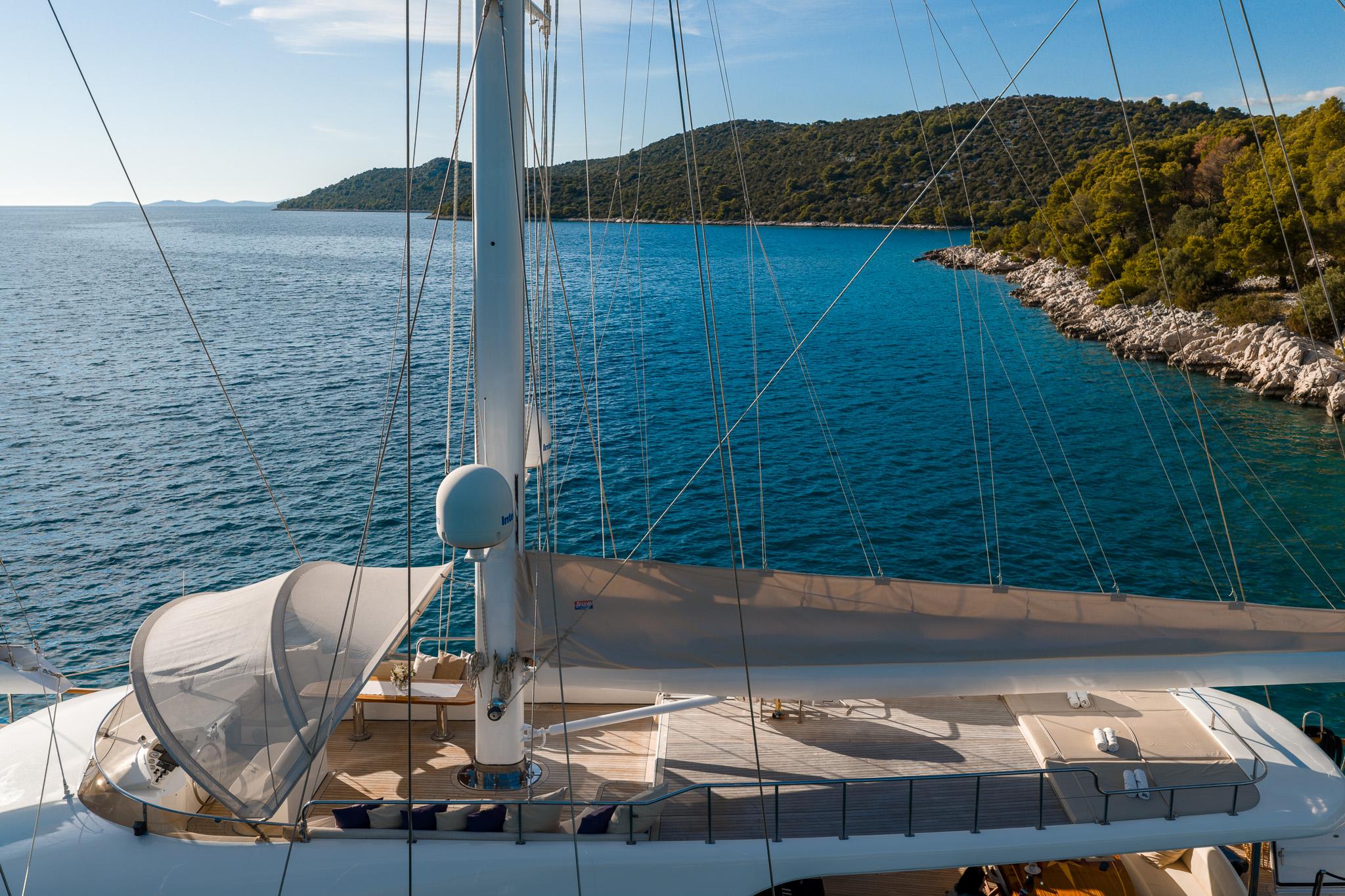 yacht upper deck showing teak decking, white mast, rigging lines and Mediterranean coastline view