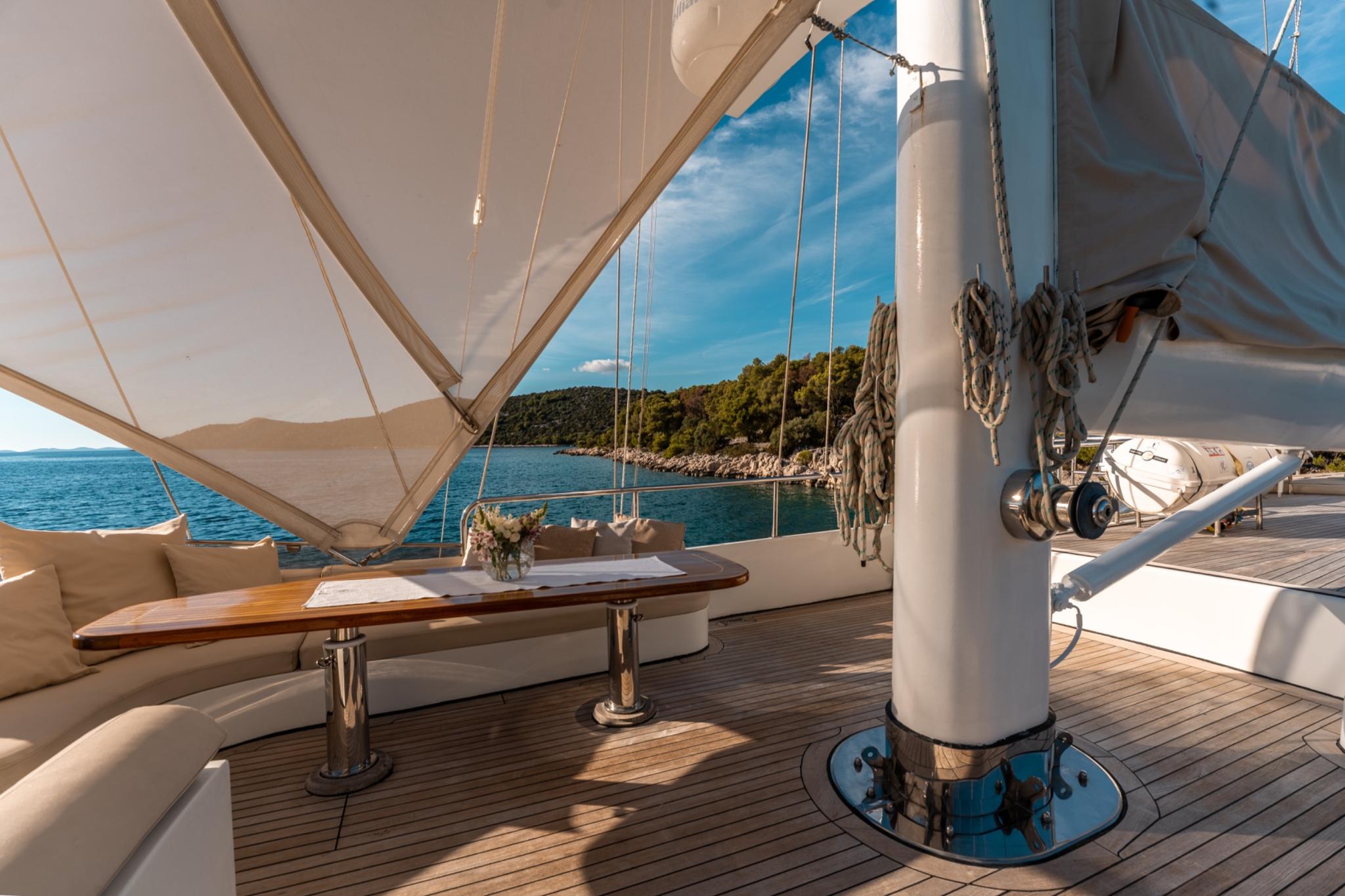 yacht aft deck with teak flooring, oval dining table, white seating and canvas awning overhead