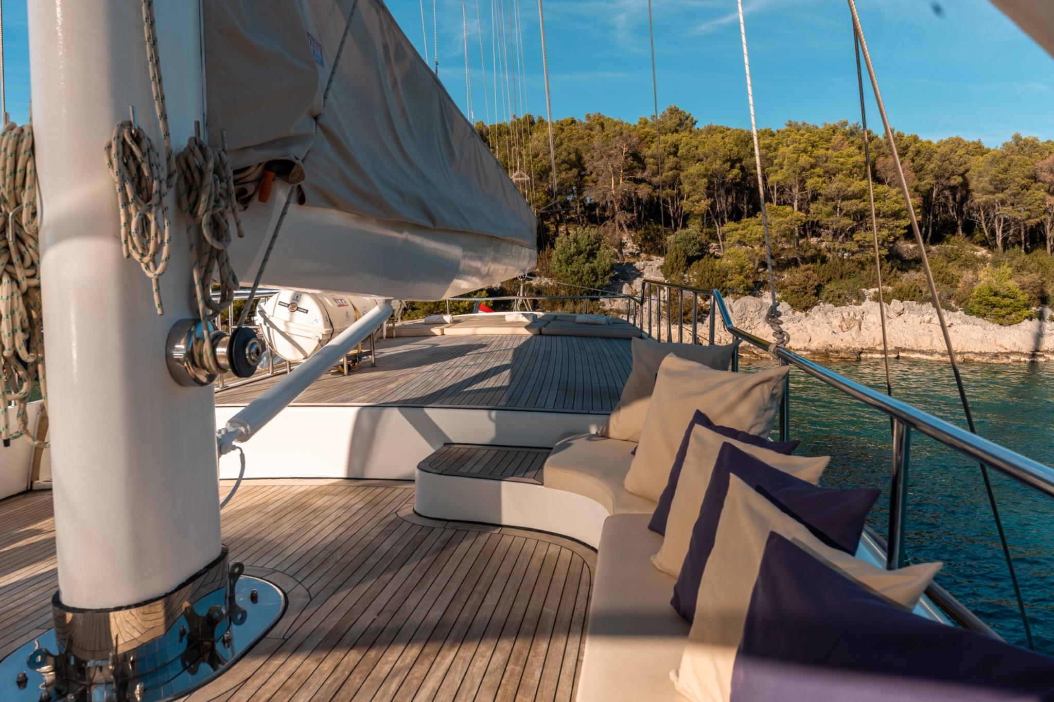 sailing yacht deck with curved seating, mast, rigging and Mediterranean coastline