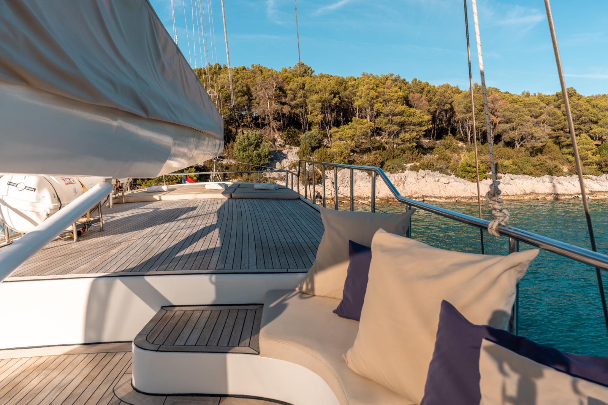 yacht aft deck with curved white seating, teak decking, stairs to upper level, anchored in bay