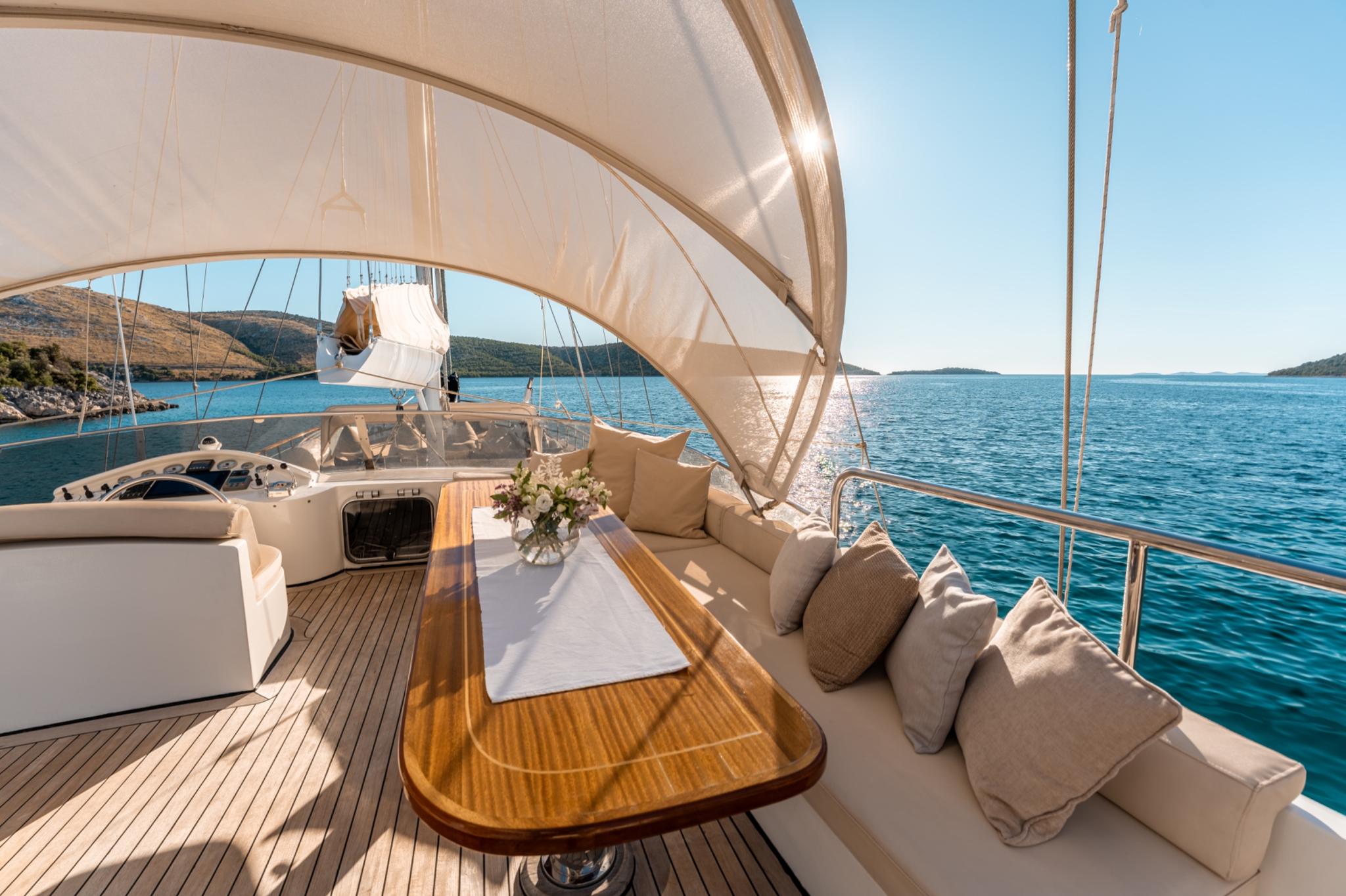 yacht main deck with curved seating, teak dining table and white sail canopy overhead