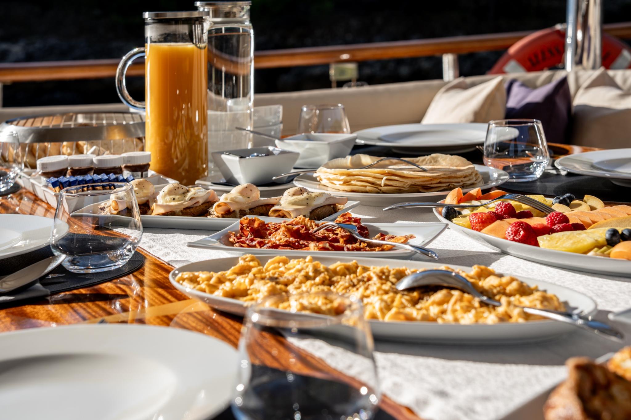 yacht breakfast table with scrambled eggs, bacon, pastries, fresh fruit and orange juice