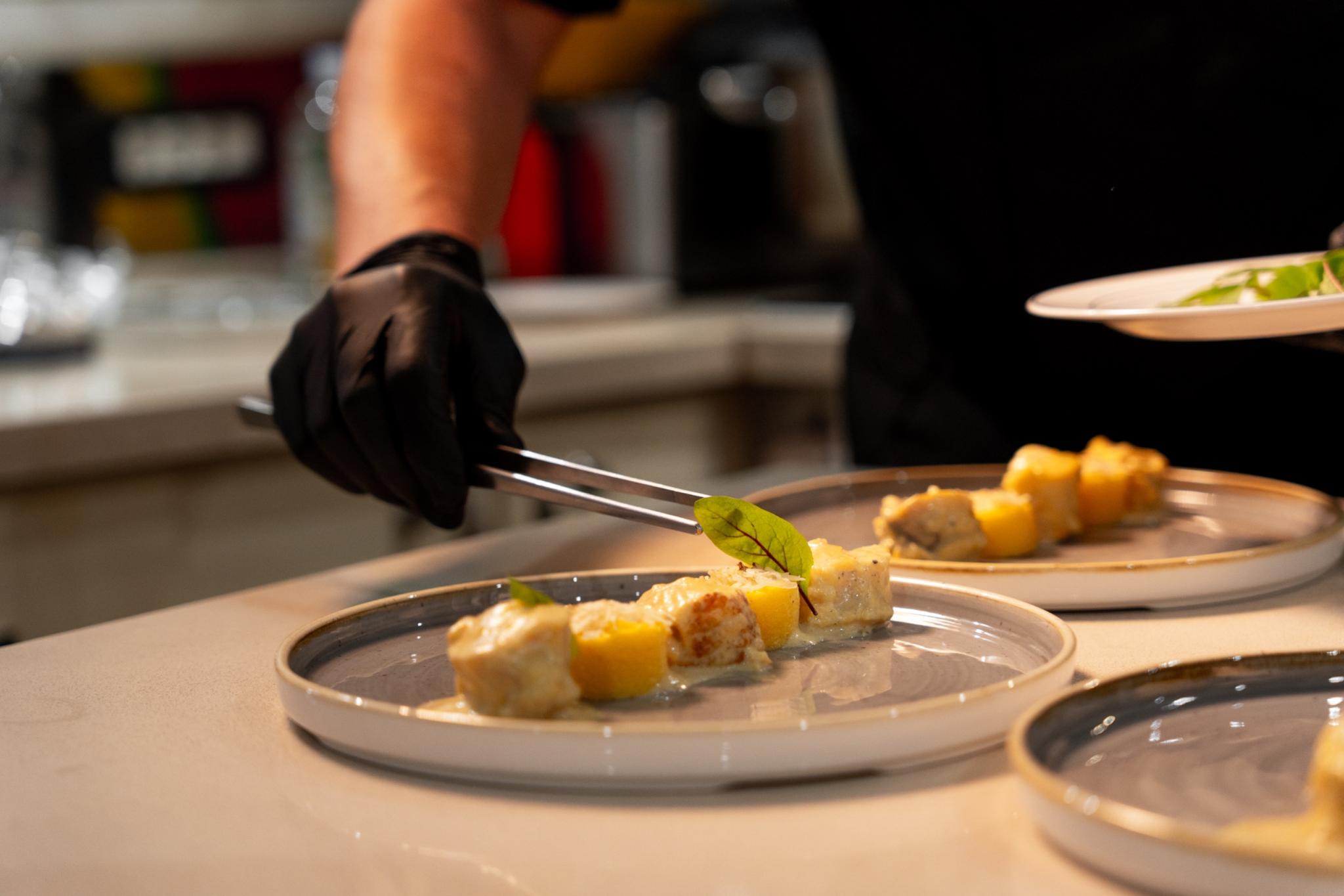 Professional chef in black gloves plating elegant appetizers with orange garnish in yacht galley