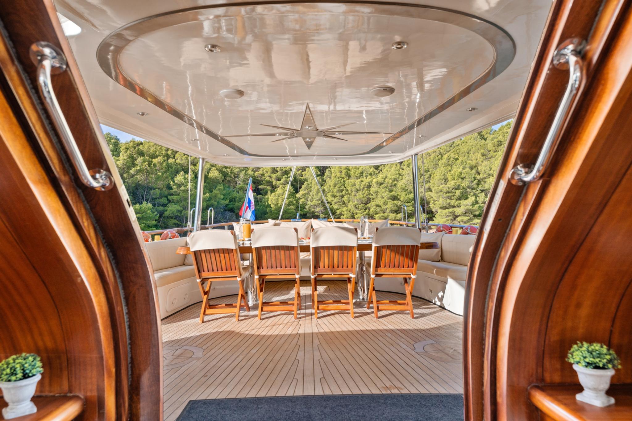 yacht aft deck with oval dining table, teak chairs and curved seating under hard top