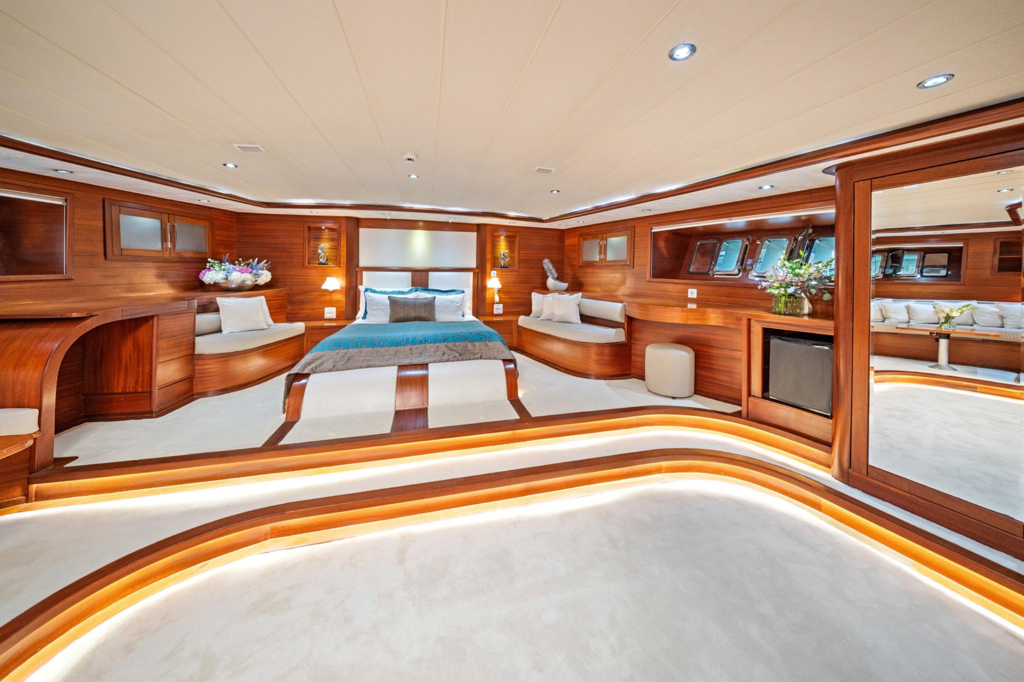 spacious master cabin featuring double bed with blue runner, curved seating areas, and rich wood paneling