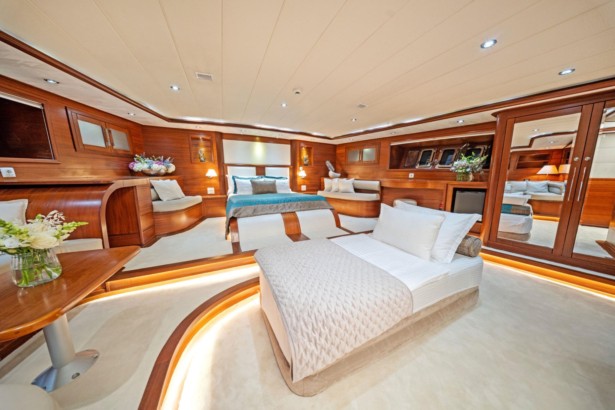luxury yacht master cabin with two double beds, rich wood paneling and built-in seating