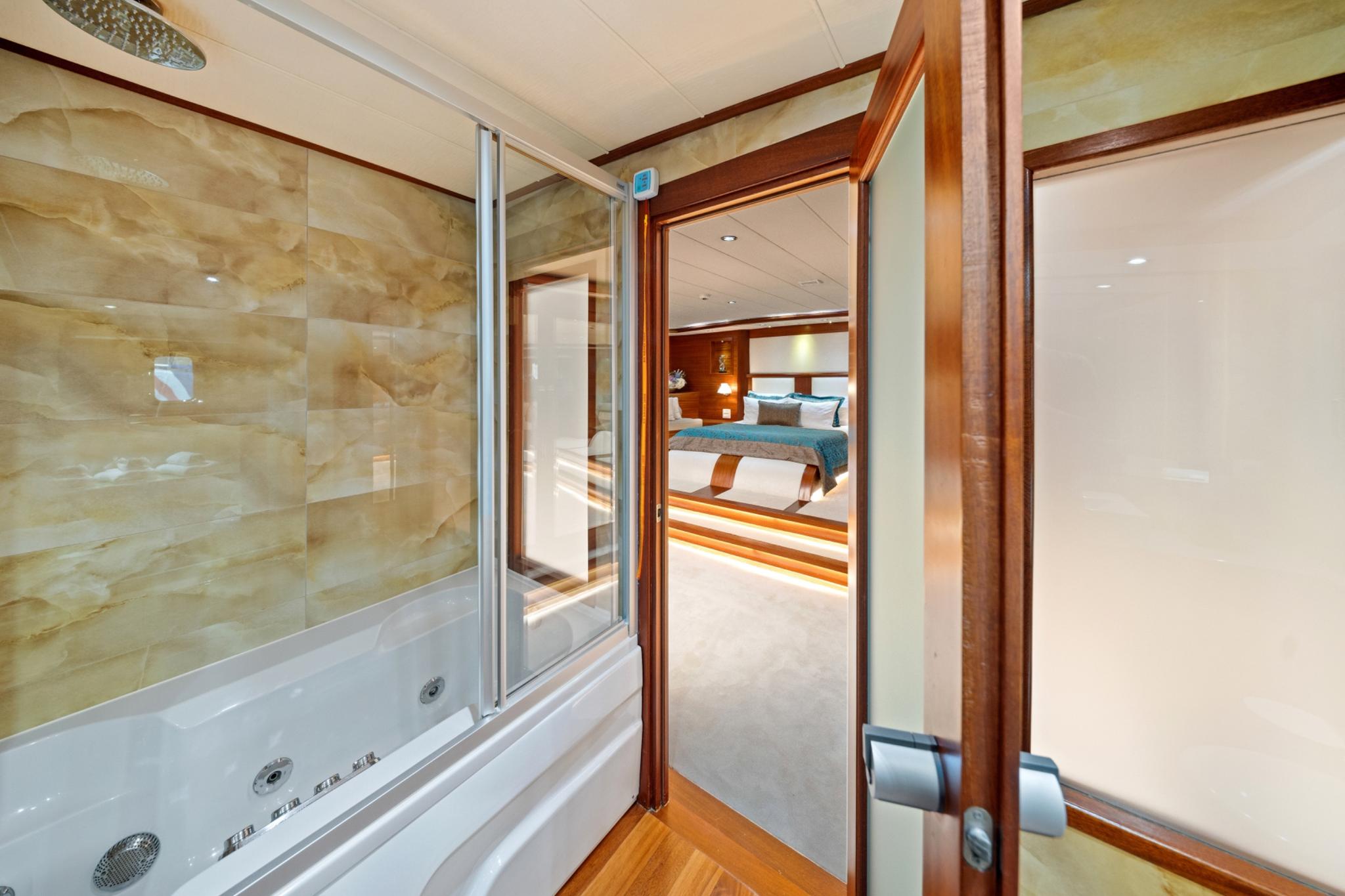 yacht cabin ensuite bathroom featuring white jacuzzi tub with glass partition overlooking bedroom