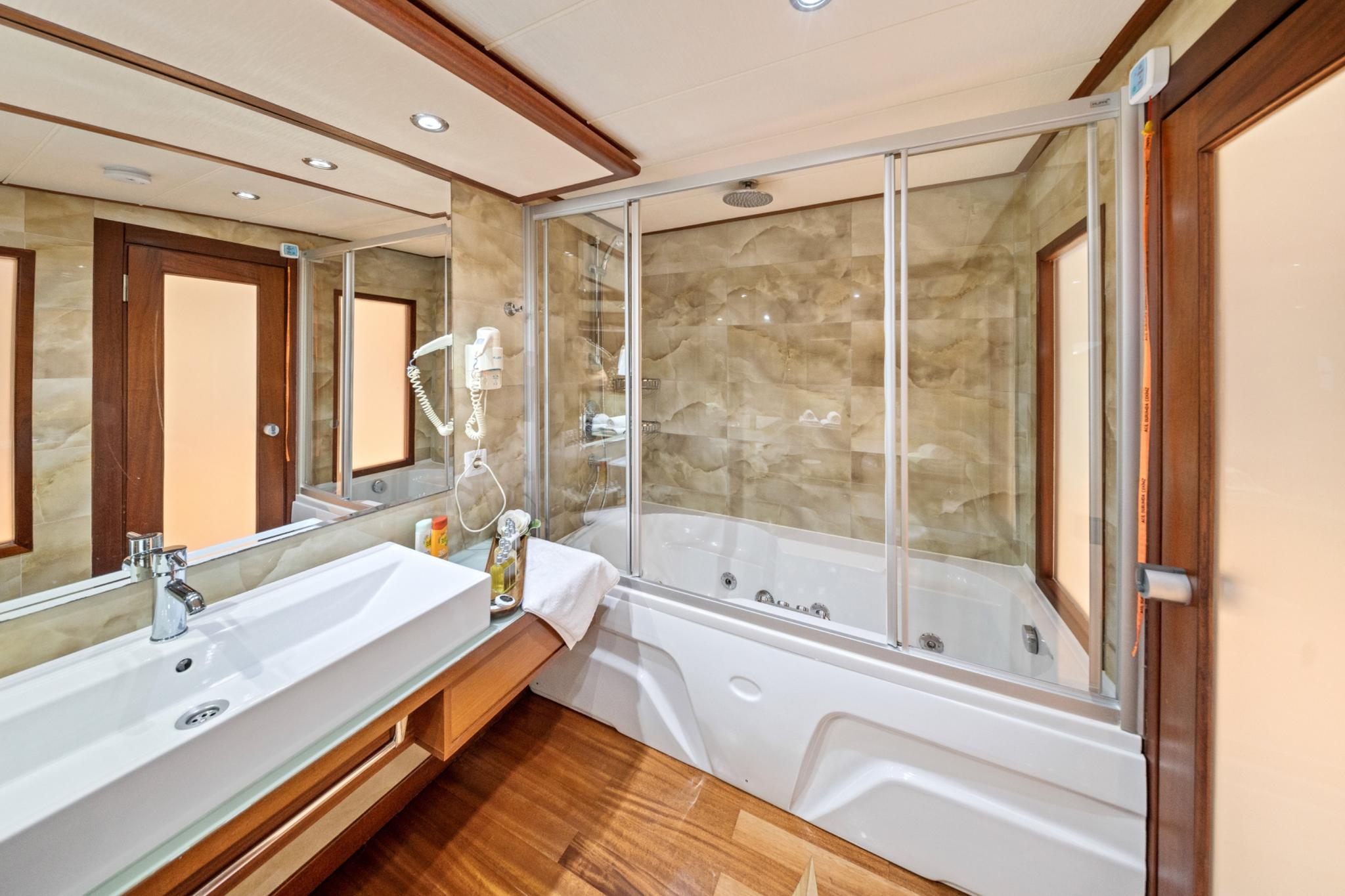 yacht bathroom featuring white jacuzzi tub, marble walls, glass shower enclosure and wooden flooring