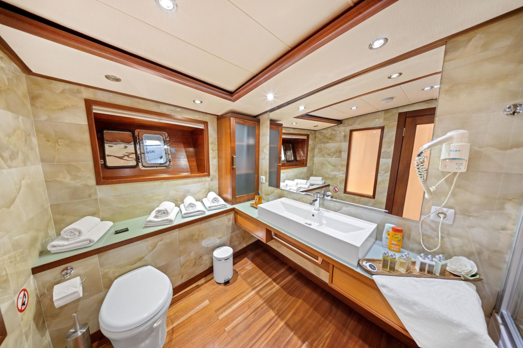Yacht en-suite bathroom with marble walls, rectangular basin, toilet and teak flooring