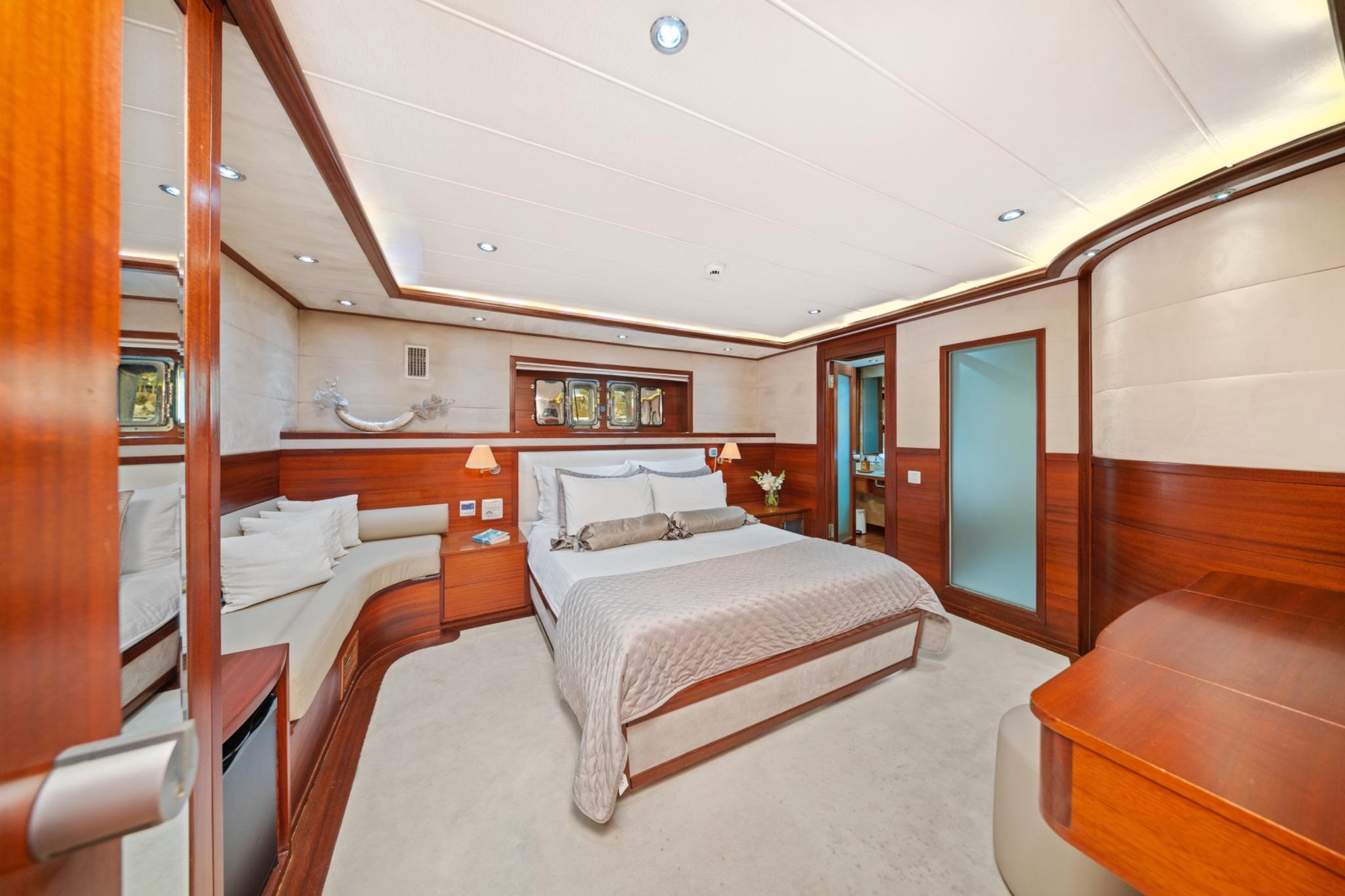 luxury yacht master cabin featuring king bed, rich wood paneling, recessed lighting and ensuite bathroom entrance