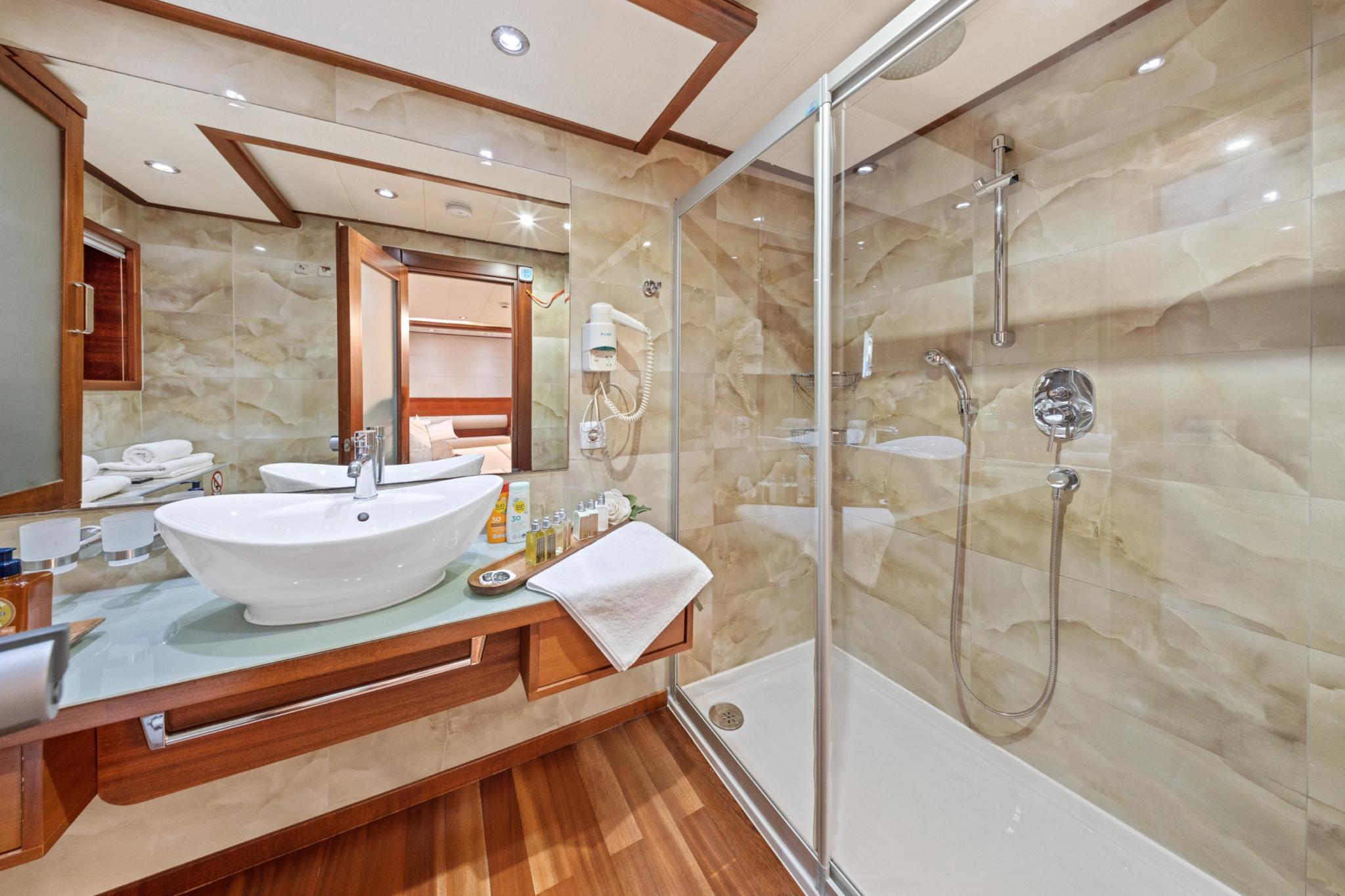 luxury yacht bathroom with marble shower enclosure, white vessel sink and wood vanity