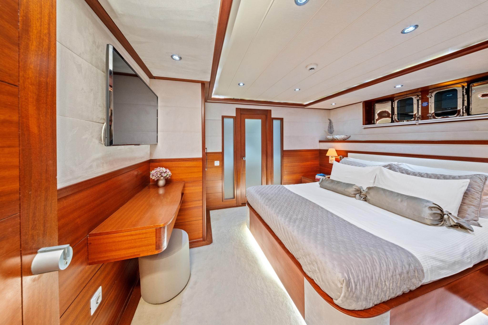 yacht guest cabin featuring double bed with gray bedding, built-in wooden desk, and frosted glass door