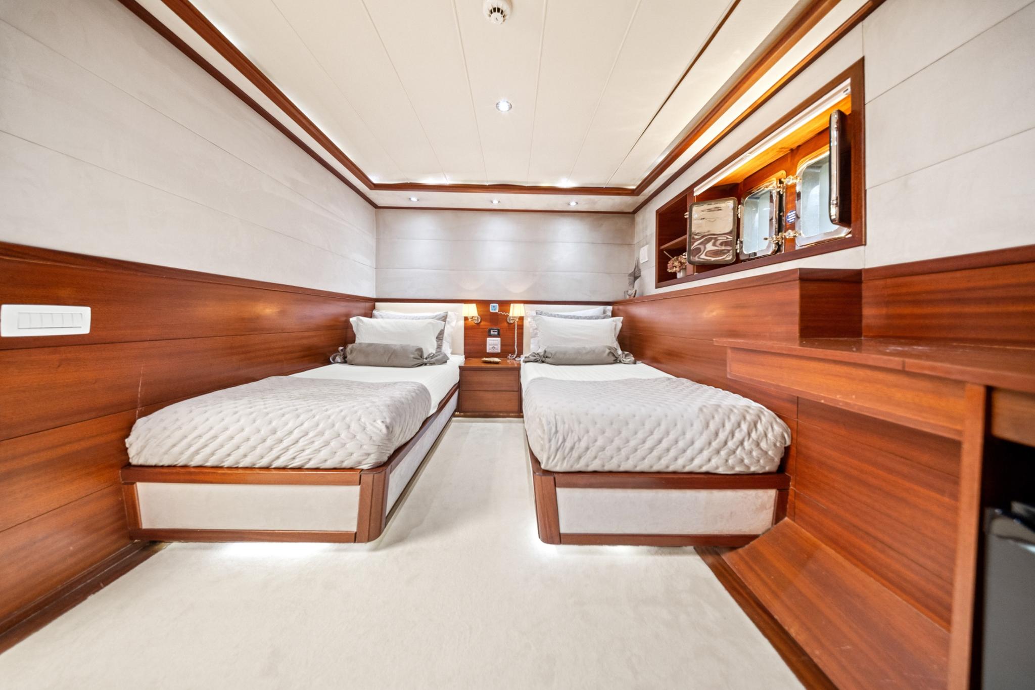 Twin cabin interior with two single beds, wood paneling, white linens and recessed lighting