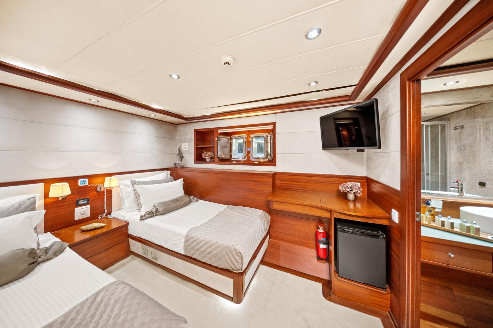 yacht cabin featuring double bed, wood paneling, wall-mounted TV and en-suite bathroom entrance