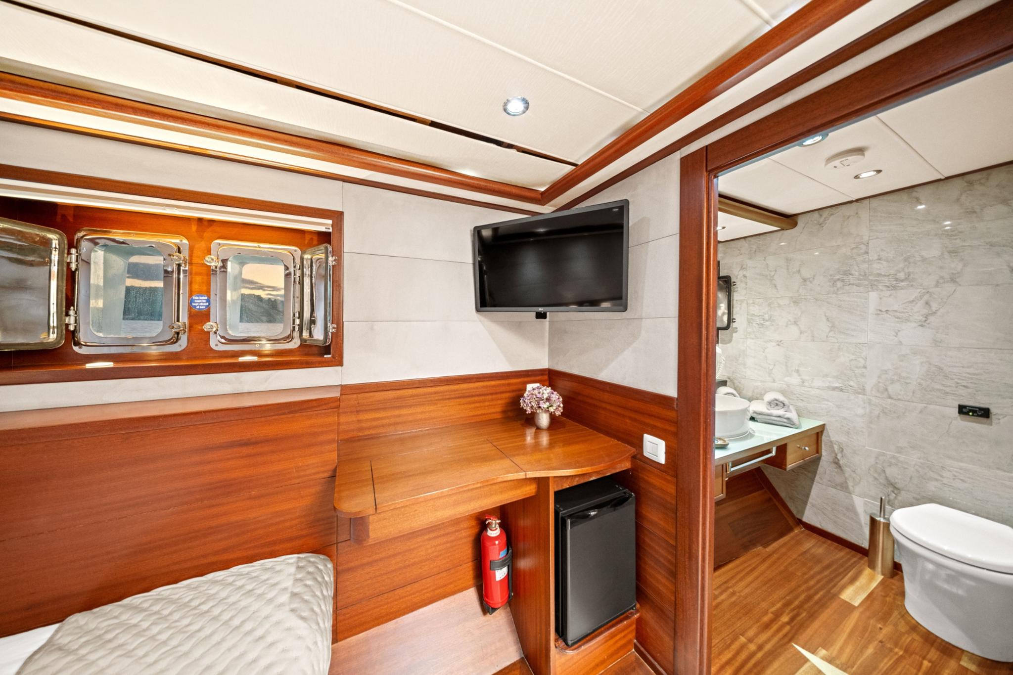 yacht cabin with wooden paneling, wall-mounted TV, portholes and marble en-suite bathroom