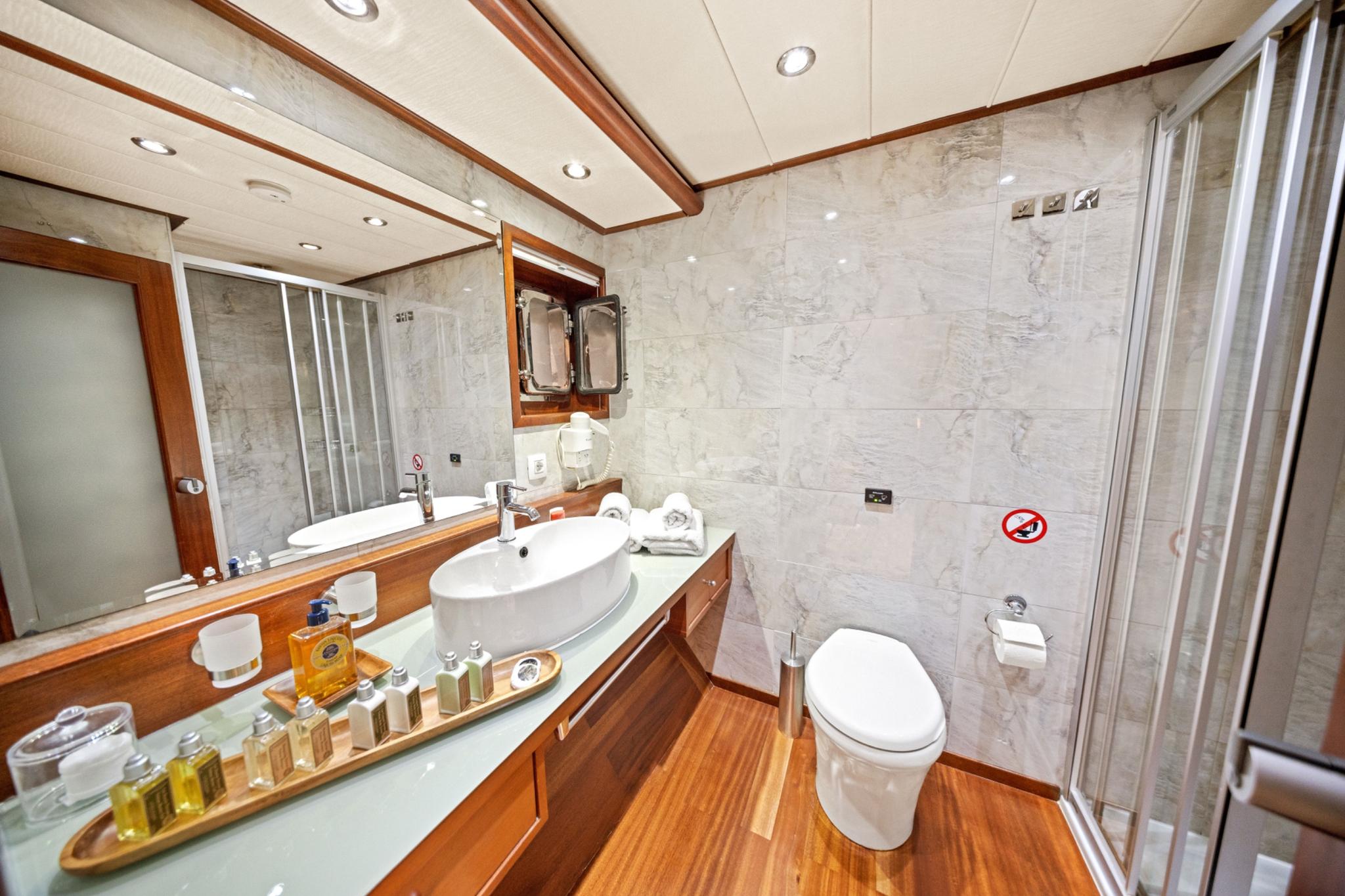 elegant yacht bathroom featuring marble walls, oval basin, teak flooring and glass shower