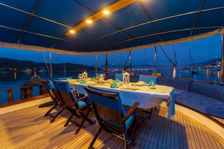 gulet aft deck with white tablecloth dining table and wooden chairs at evening twilight